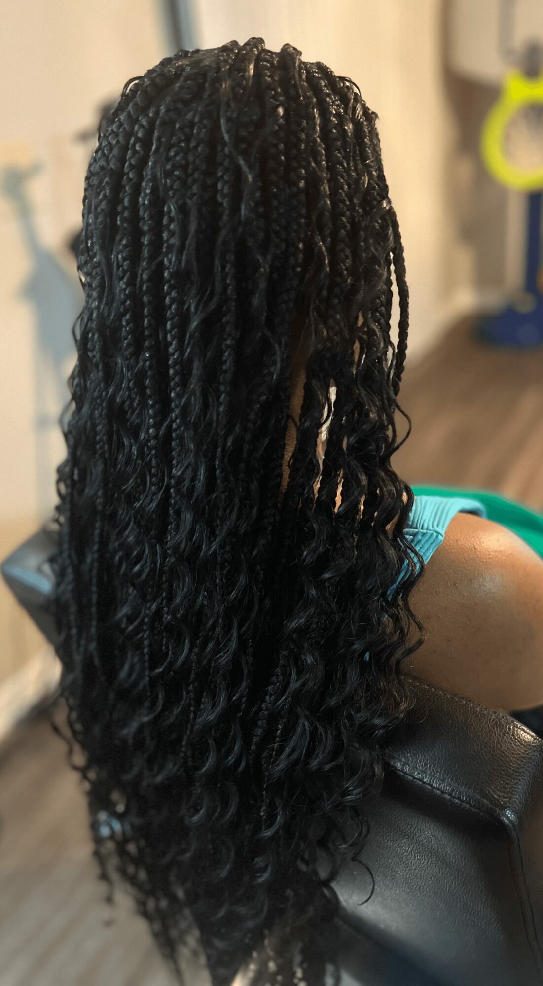 Back view of long, curly, braided hairstyle on a person sitting in a chair indoors.