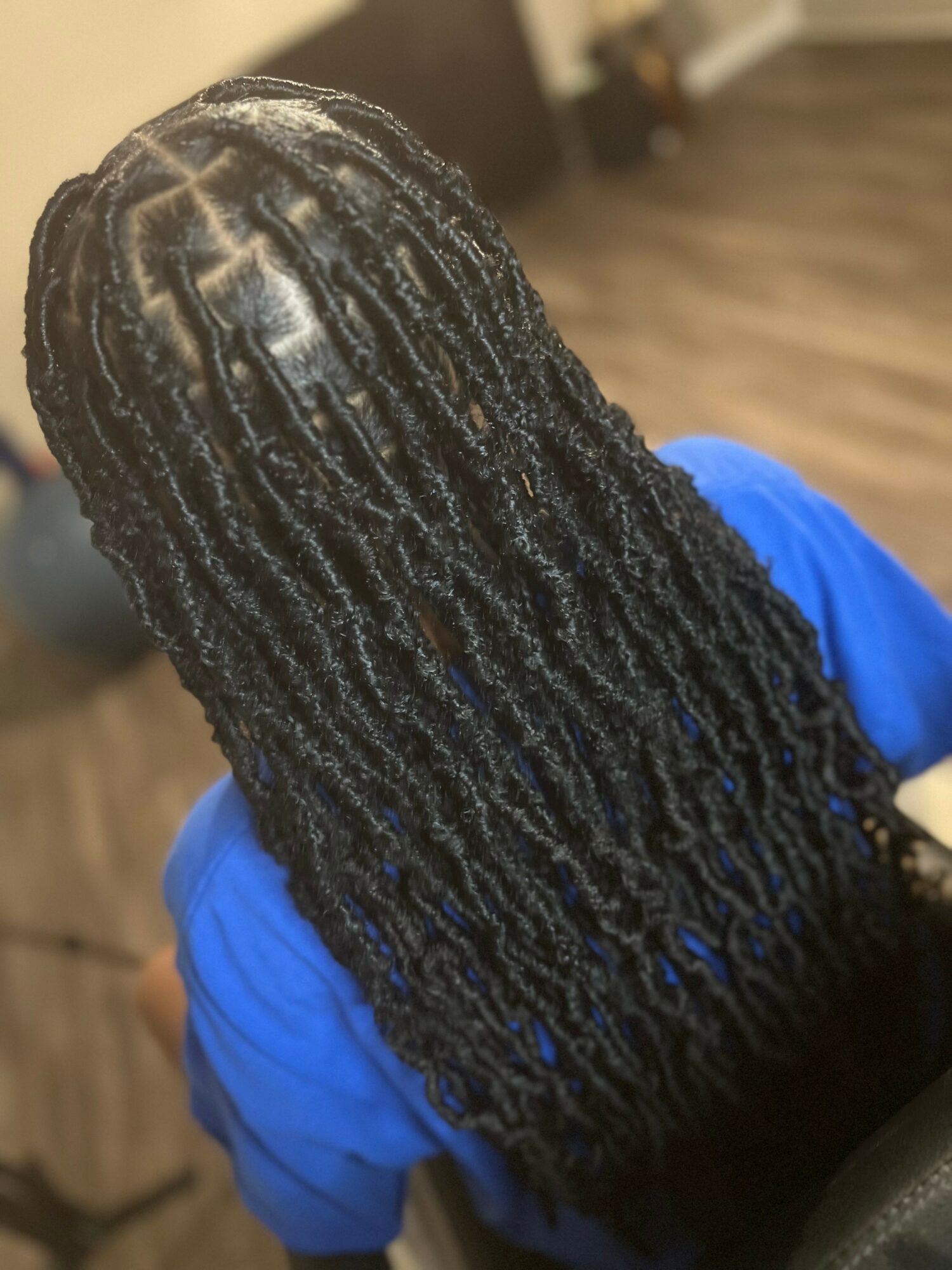 Person with long, styled dreadlocks wearing a blue shirt, viewed from behind in an indoor setting.