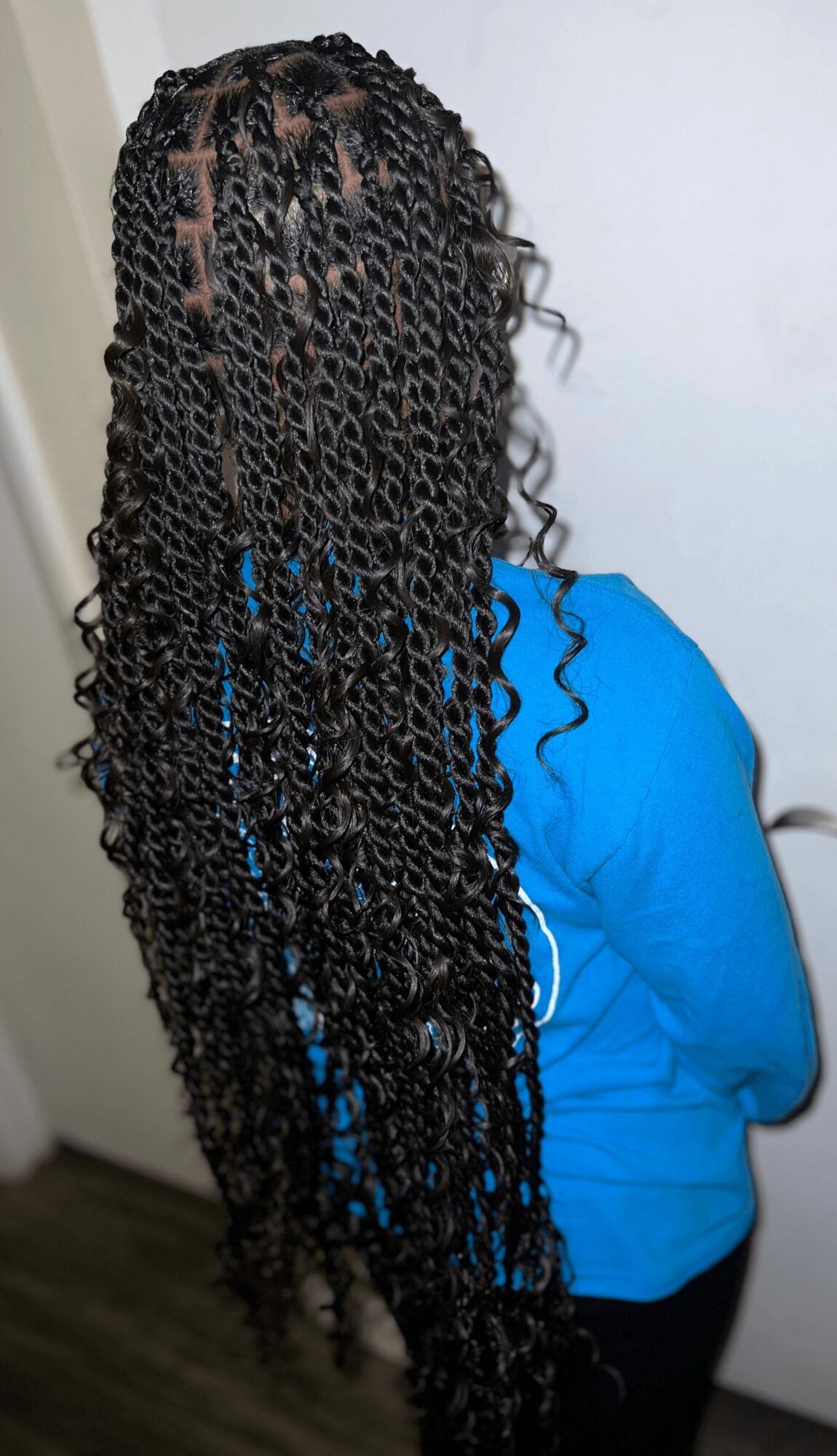 Person with long, curly hair wearing a blue top, facing away from the camera, standing indoors.