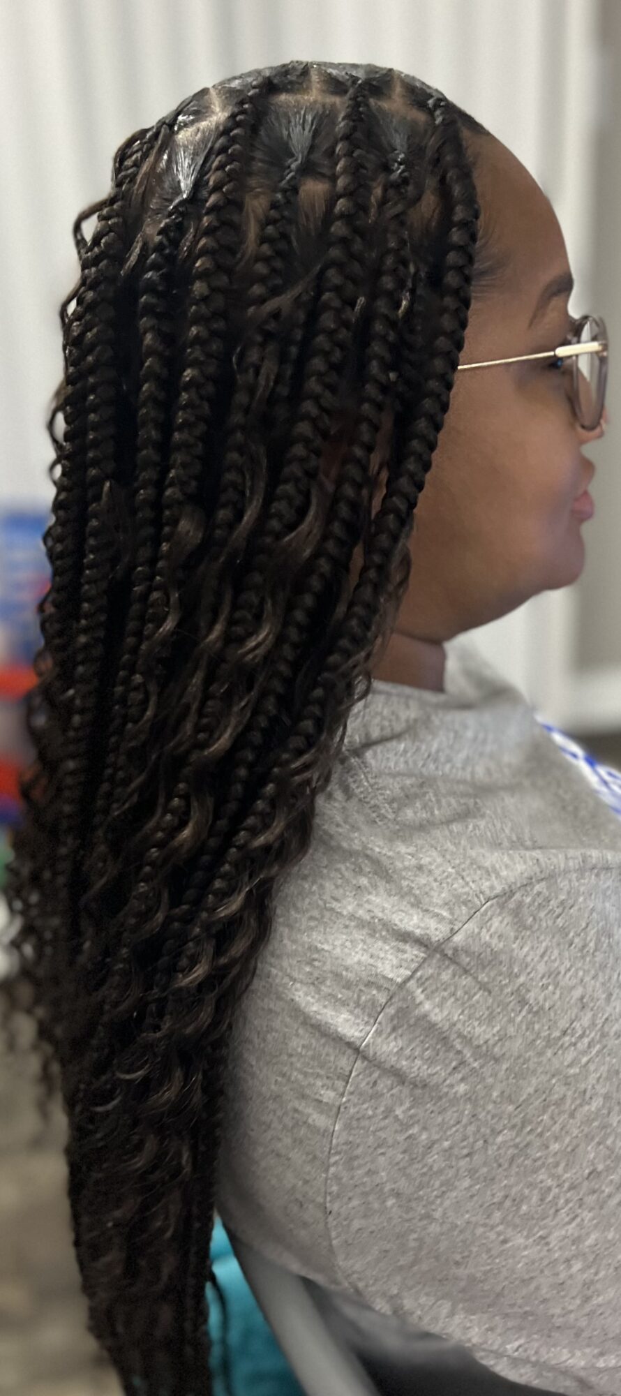 Profile of a person with long, twisted braids wearing glasses and a gray top.
