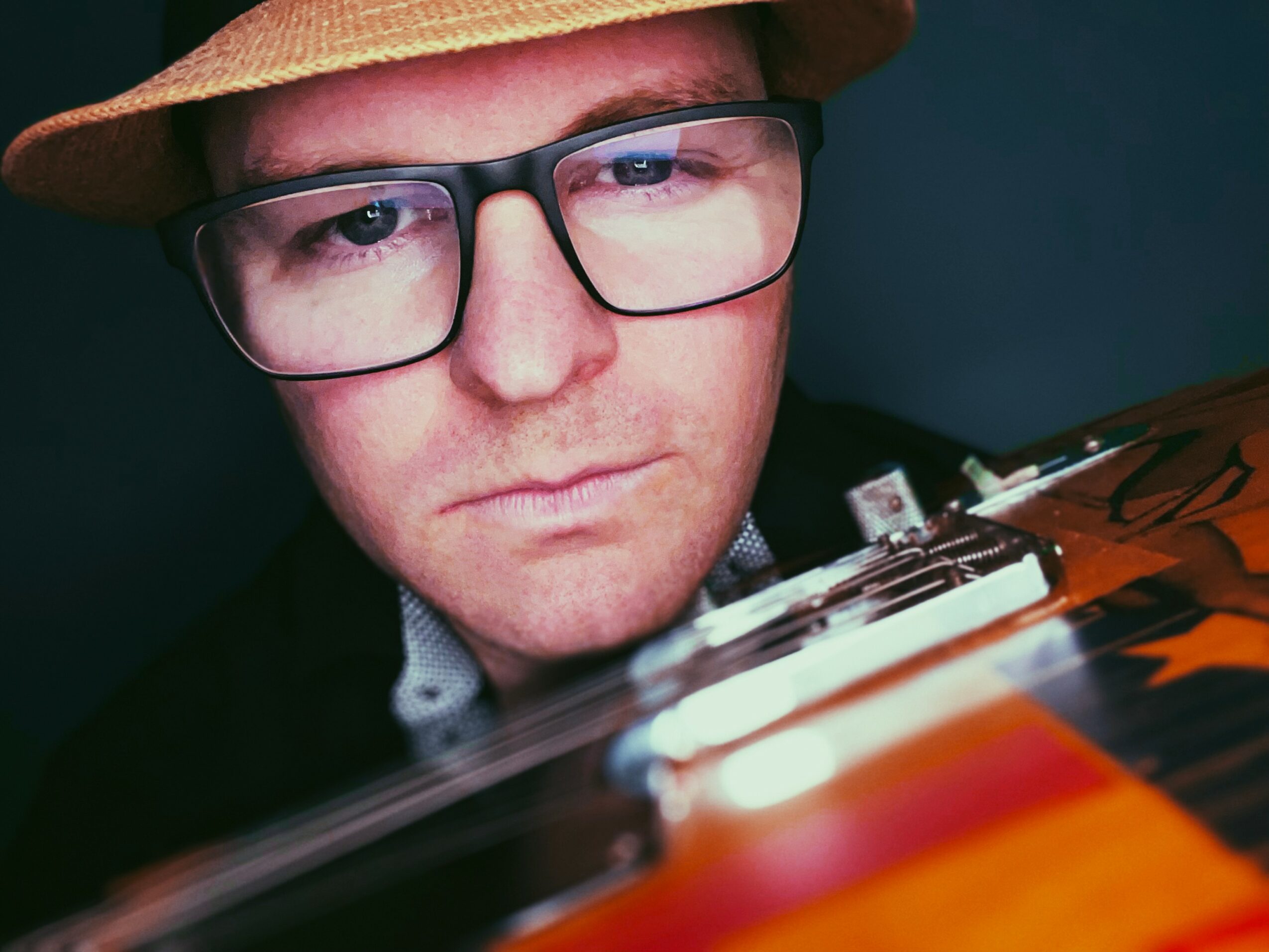 Close-up of a person wearing glasses and a hat, looking at a colorful object or instrument.