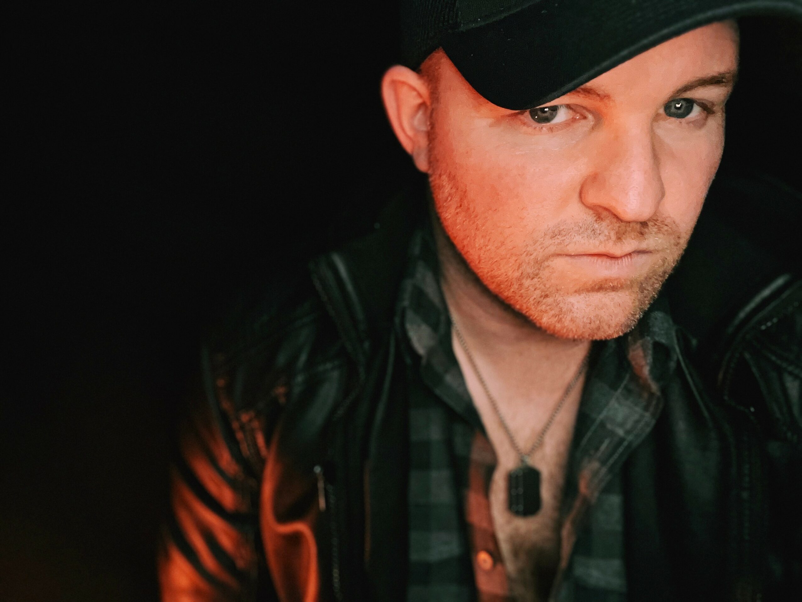 Man wearing a black cap and leather jacket, looking at the camera with a serious expression.