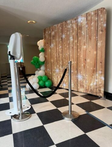Decorative backdrop with balloons and a starry pattern, set up behind a black and white checkered floor, with stanchions and a velvet rope.