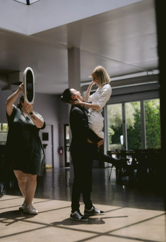 Two people, one holding a child, are in a spacious room with large windows and natural light.