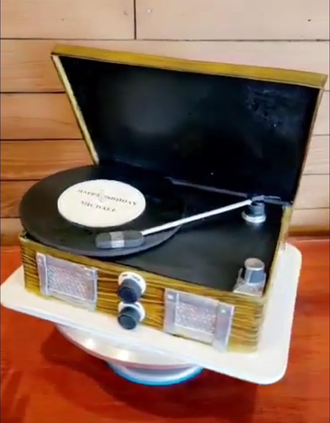 Vintage record player with open lid, turntable, and control knobs, placed on a white surface against a wooden background.