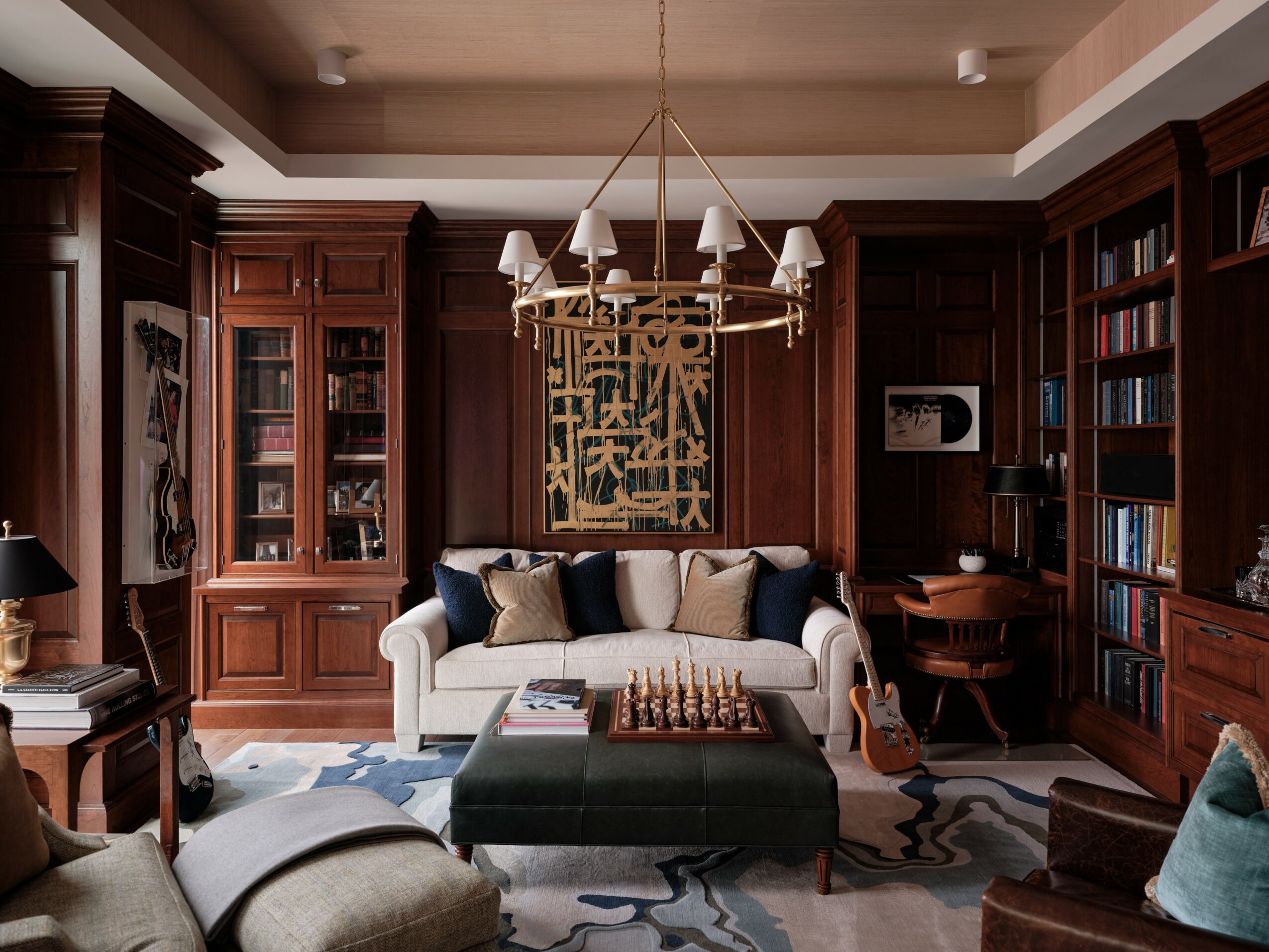 Living room with a white sofa, dark wood bookshelves, a chandelier, and a chessboard on an ottoman, with a guitar nearby.