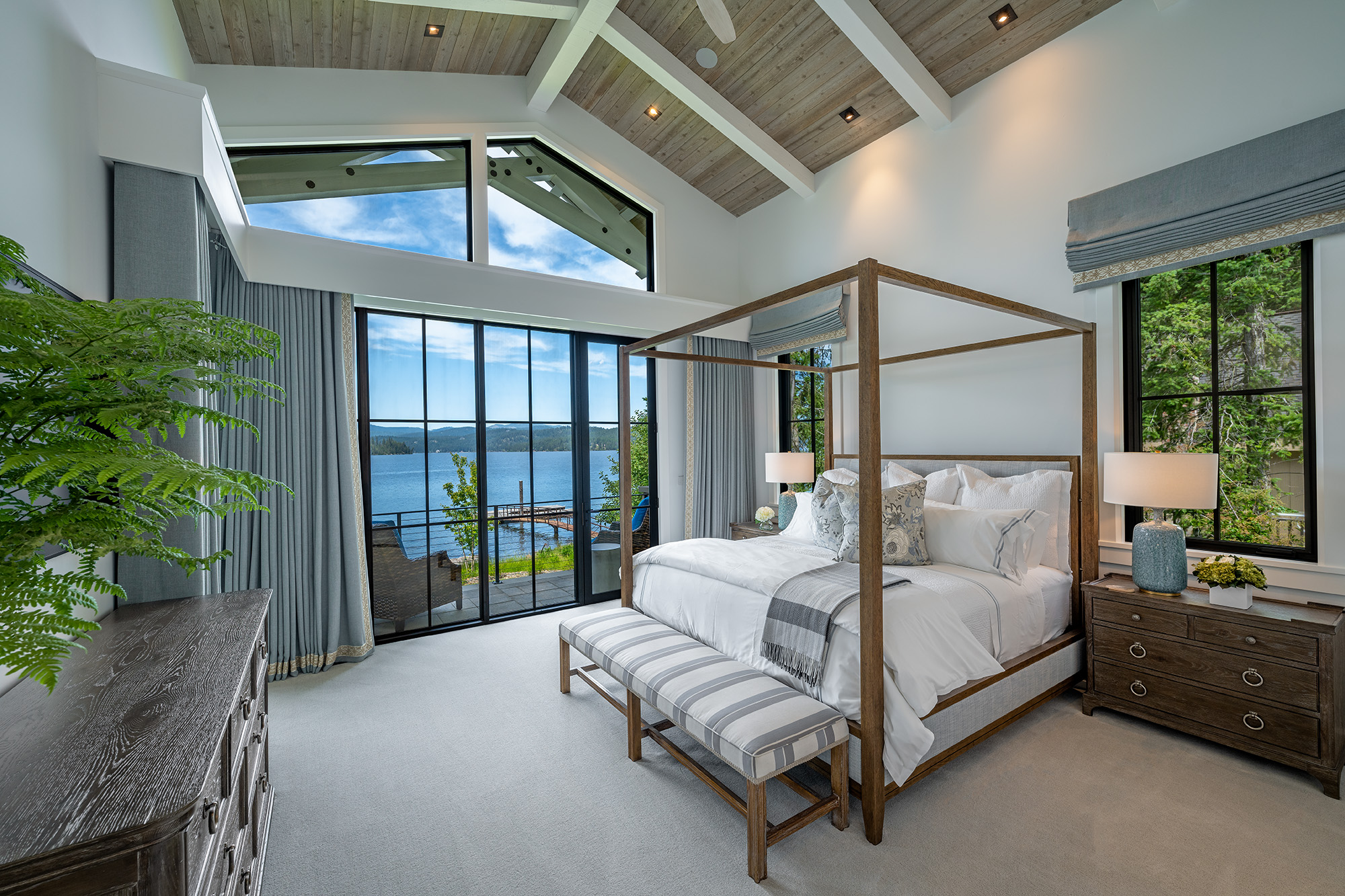 Bedroom with a four-poster bed, large windows showing a view of water, and a bench at the foot of the bed.