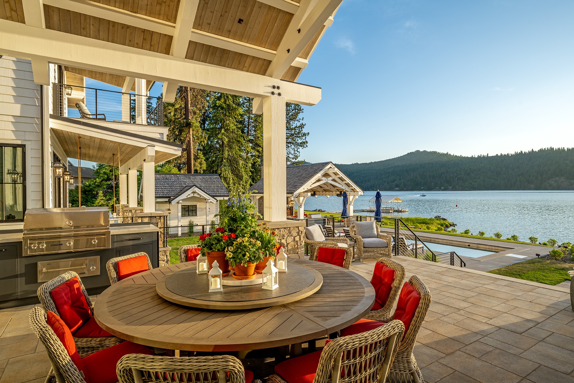 Outdoor patio with round table, red chairs, and a view of a lake and mountains in the background.