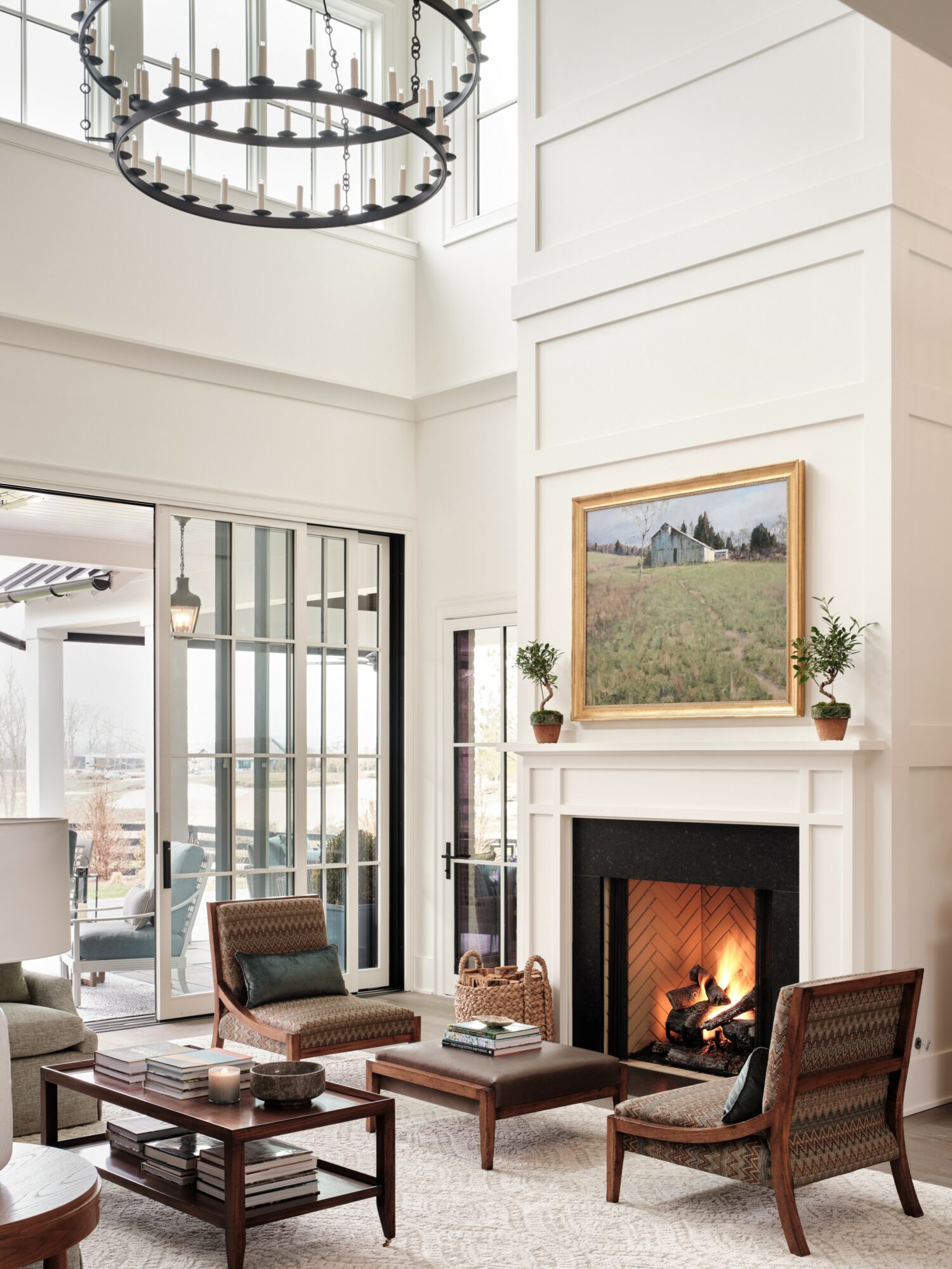 Living room with fireplace, large window, and seating area, decorated in neutral tones with a chandelier overhead.