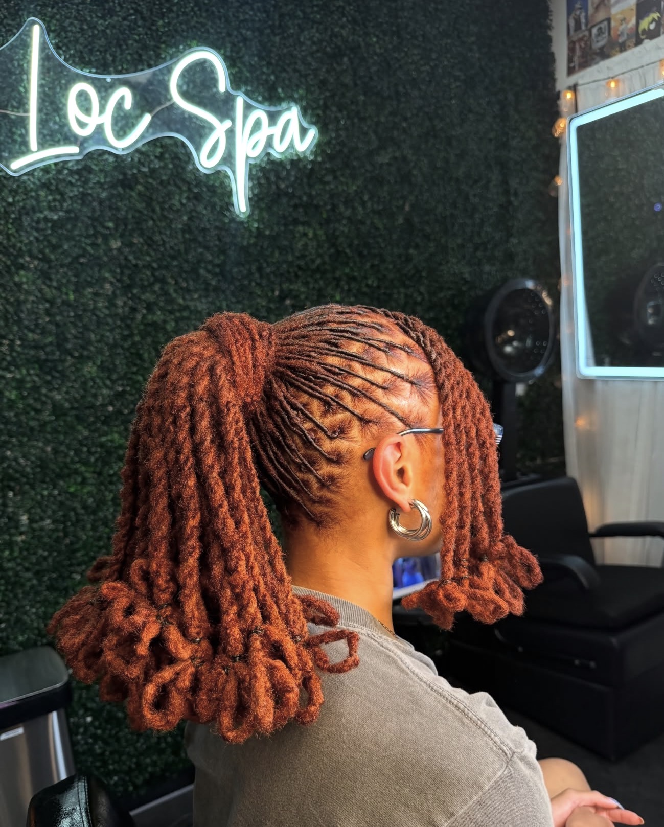 Person with orange dreadlocks sitting in a salon, neon sign reads 'Loc Spa' in the background.