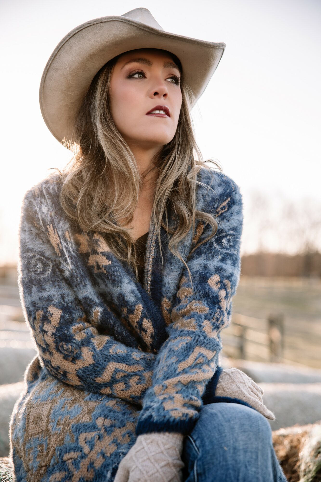 Woman wearing a large hat and patterned sweater outdoors, looking to the side with a neutral expression.