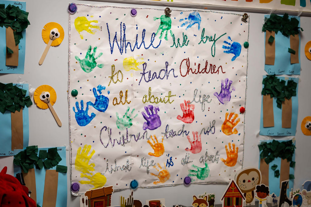 Decorated classroom wall with a poster, colorful handprints, and paper trees, celebrating teaching children.