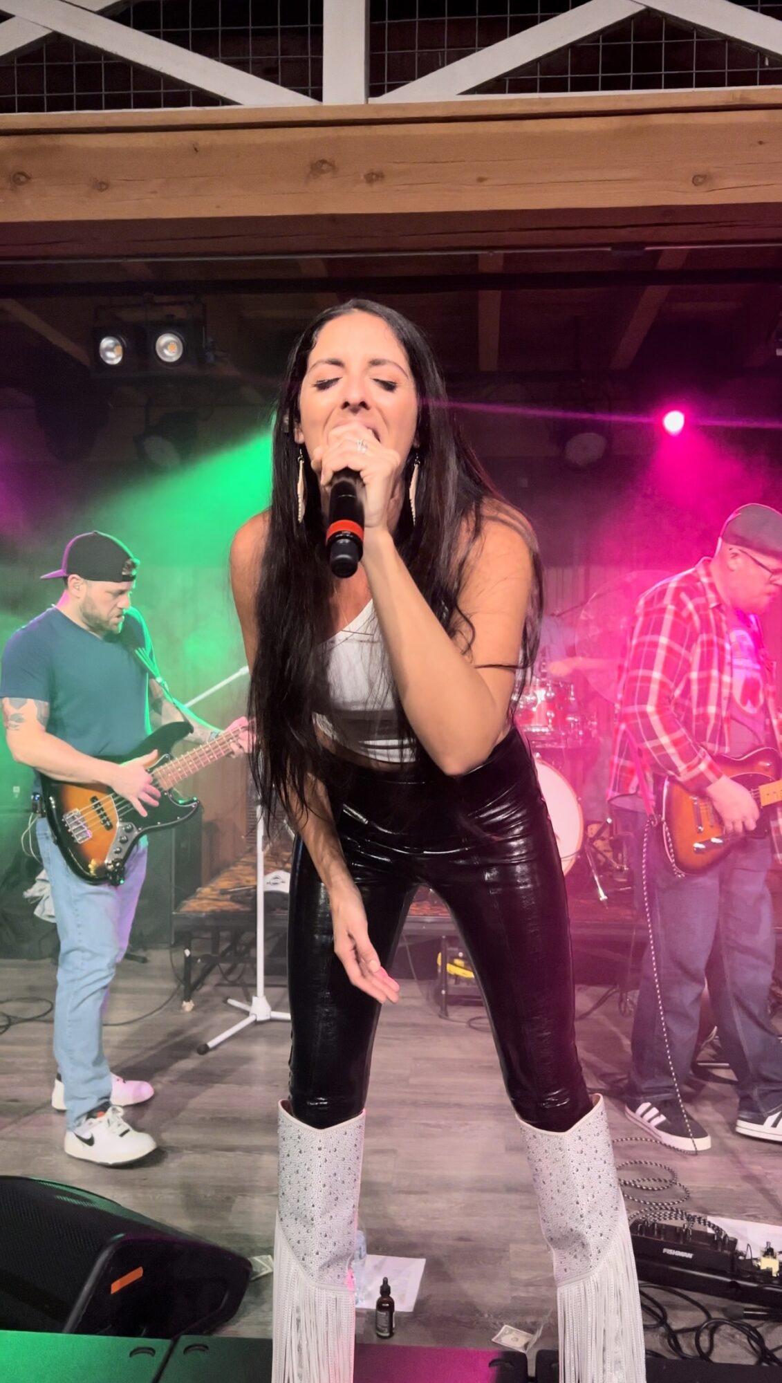 Female singer with long dark hair performs on stage with band, colorful lights in background.