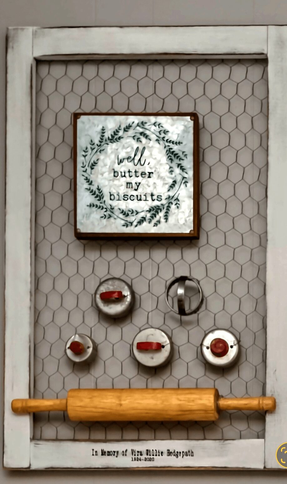 Decorative display with a framed cross-stitch pattern, six small jars, and a wooden rolling pin, set against a honeycomb background.