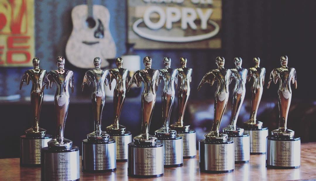 Eight identical trophies with a figure holding a trophy, lined up on a surface, with a blurred background.