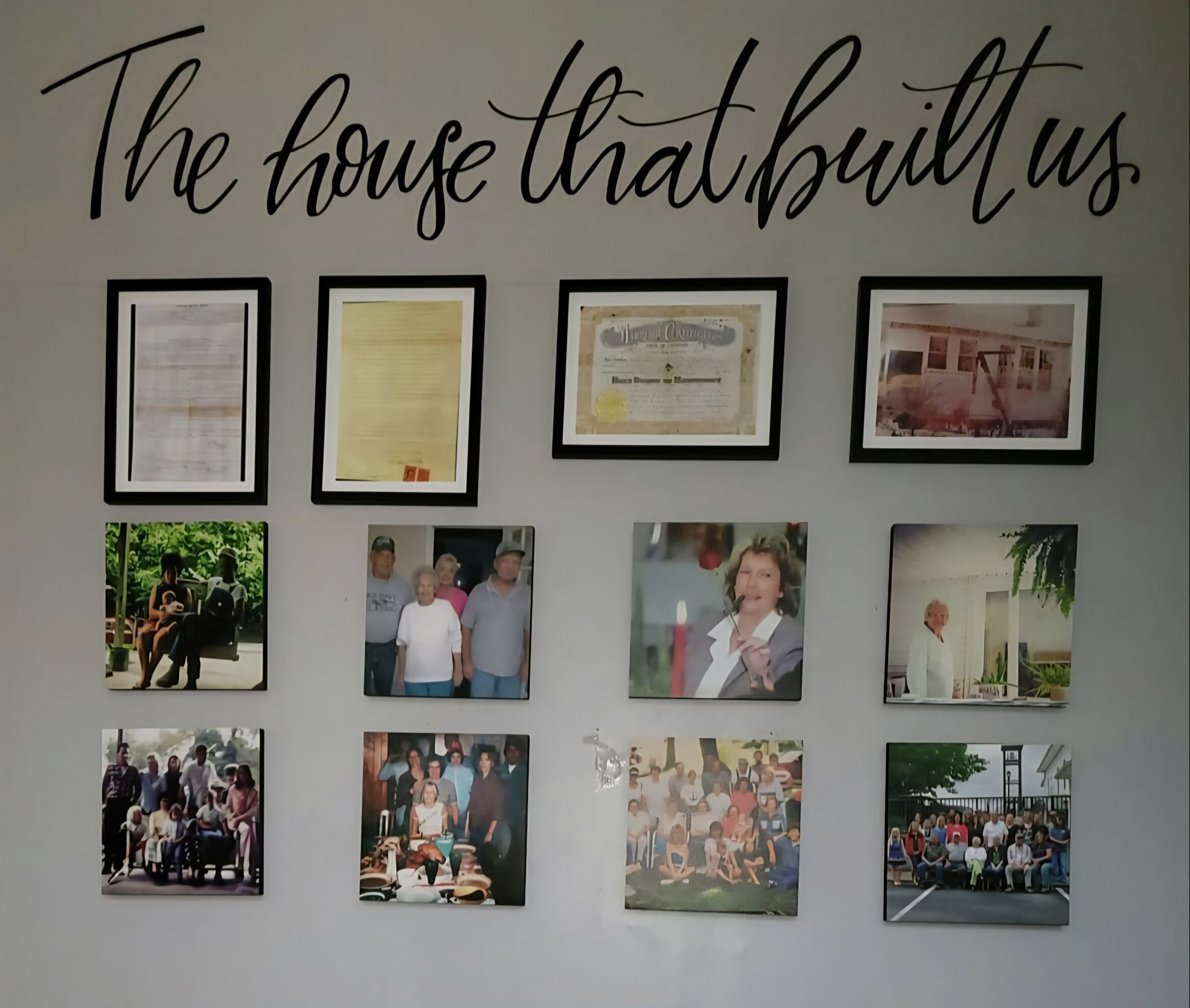 Wall display with framed documents and photos, including a group of people outdoors and a woman in a white shirt.