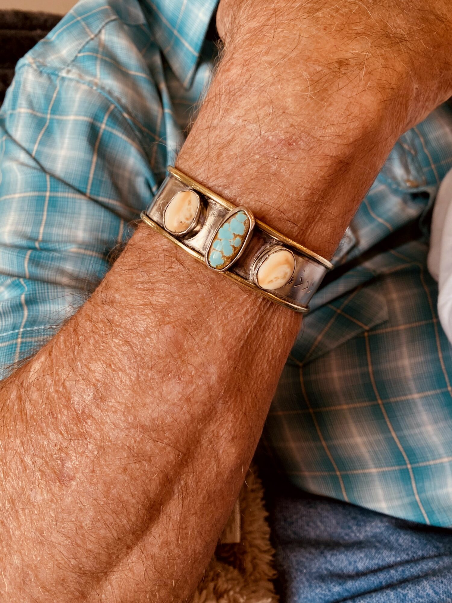 Close-up of an elderly person's arm with a bracelet featuring turquoise and shell stones, wearing a blue plaid shirt.