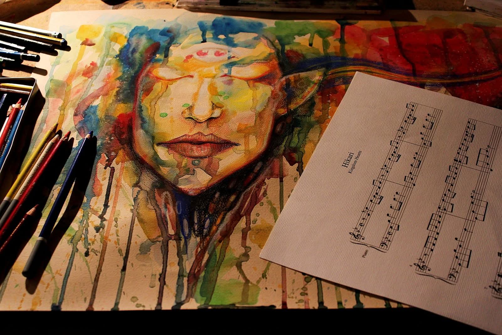 Watercolor painting of a woman's face with colorful drips, surrounded by paintbrushes and sheet music, on a wooden surface.