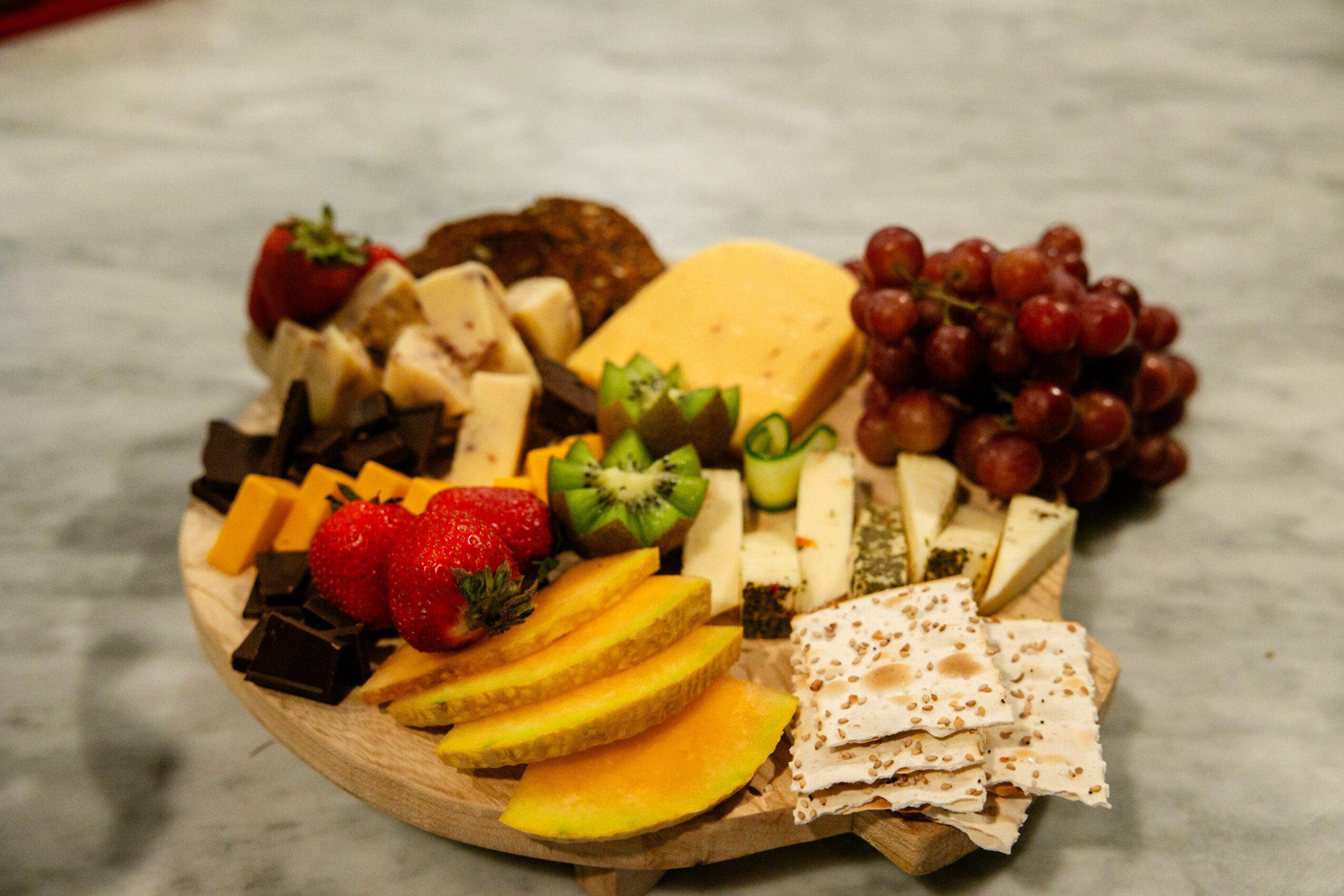 Assorted cheeses, grapes, strawberries, kiwi, chocolate, and sliced fruit on a wooden platter.