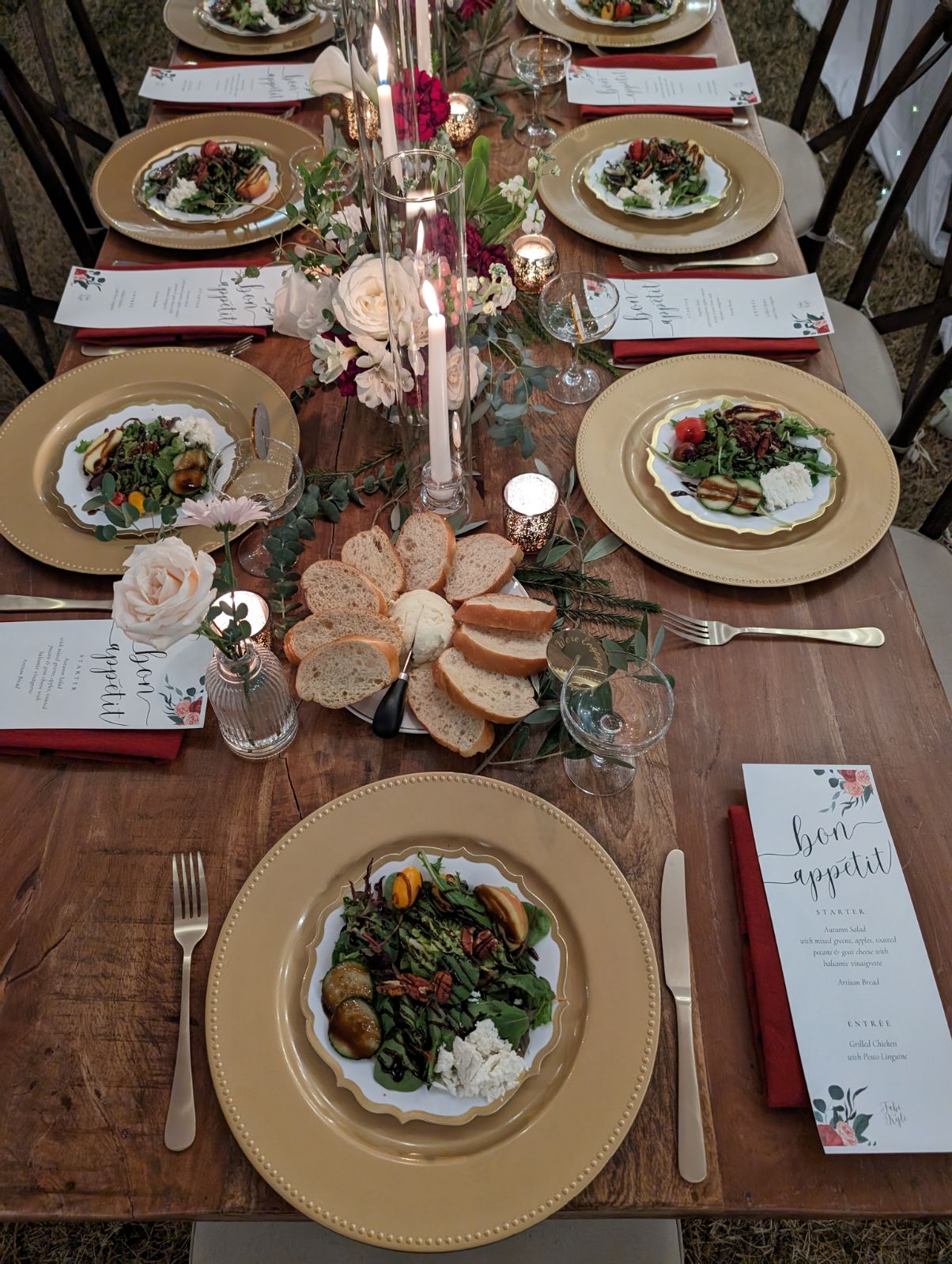 Table set with plates of salad, flowers, candles, and utensils, with a menu card on the right side.