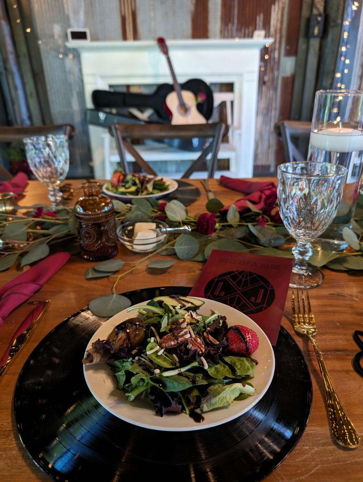 Table setting with a vinyl record plate holding a salad, glassware, and utensils, with a guitar on a stand in the background.