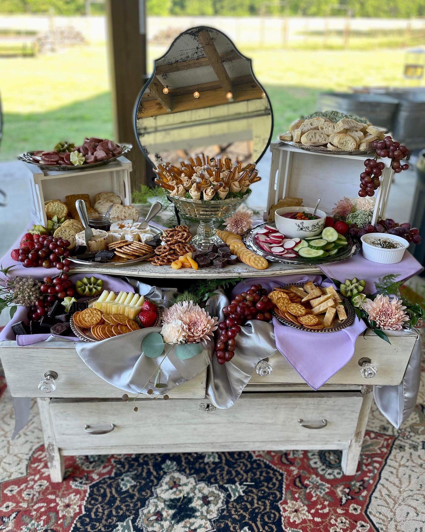 Decorative table with snacks, grapes, and flowers, set in front of a window with a grassy outdoor view.