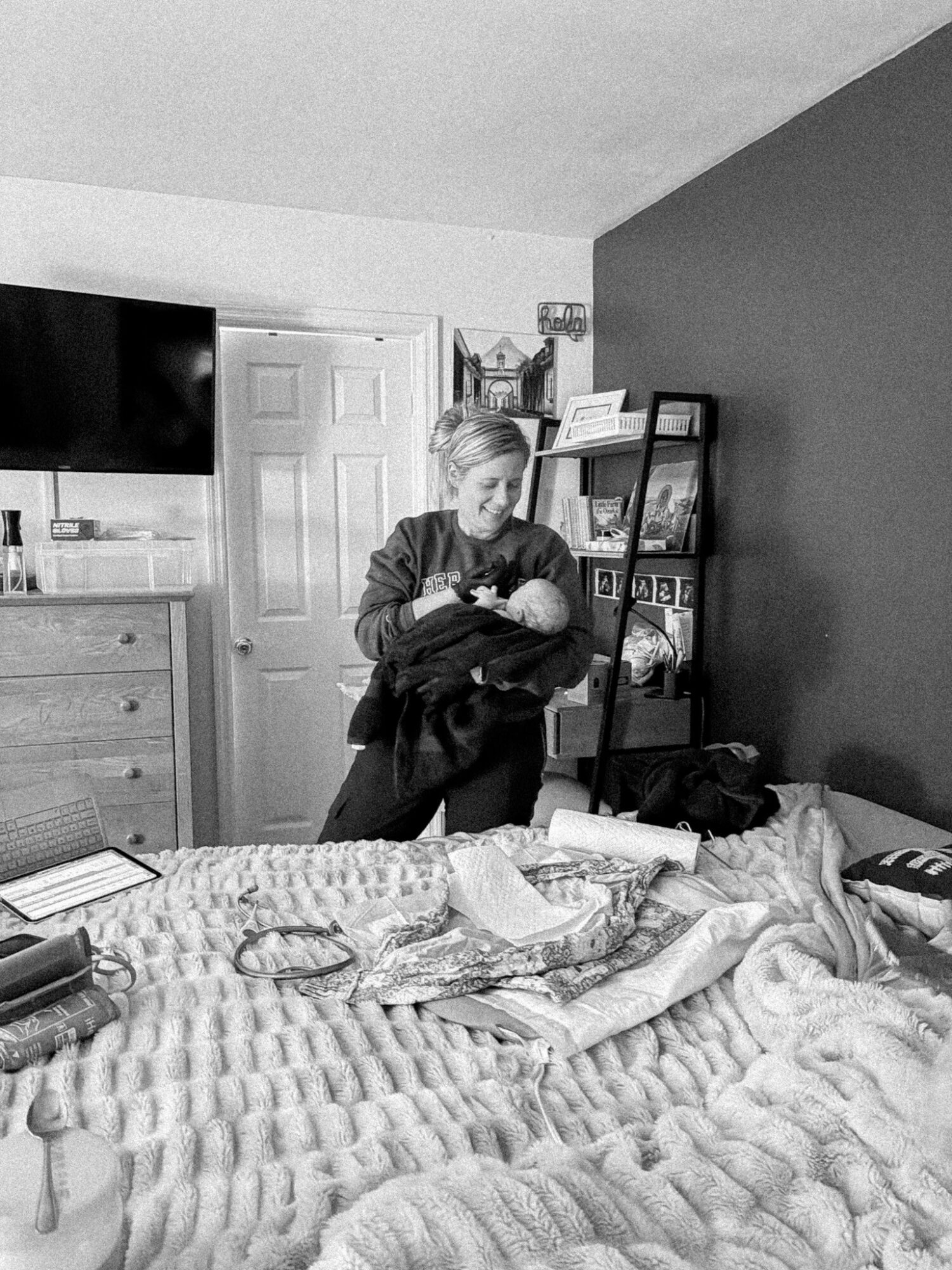 Person holding a cat in a bedroom with a bed, dresser, and bookshelf, in black and white.
