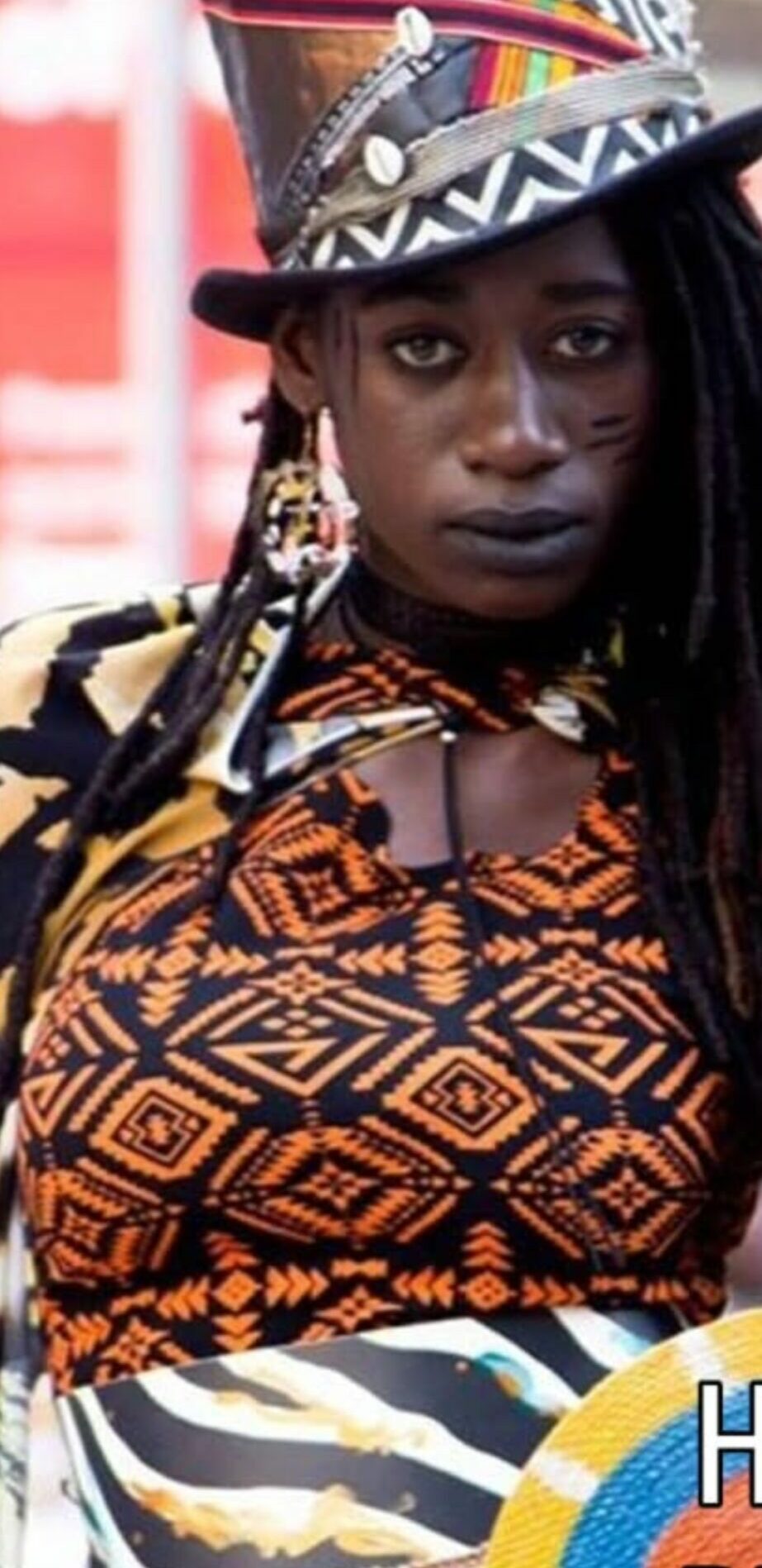 Woman wearing a patterned hat and clothing with geometric designs, looking directly at the camera.