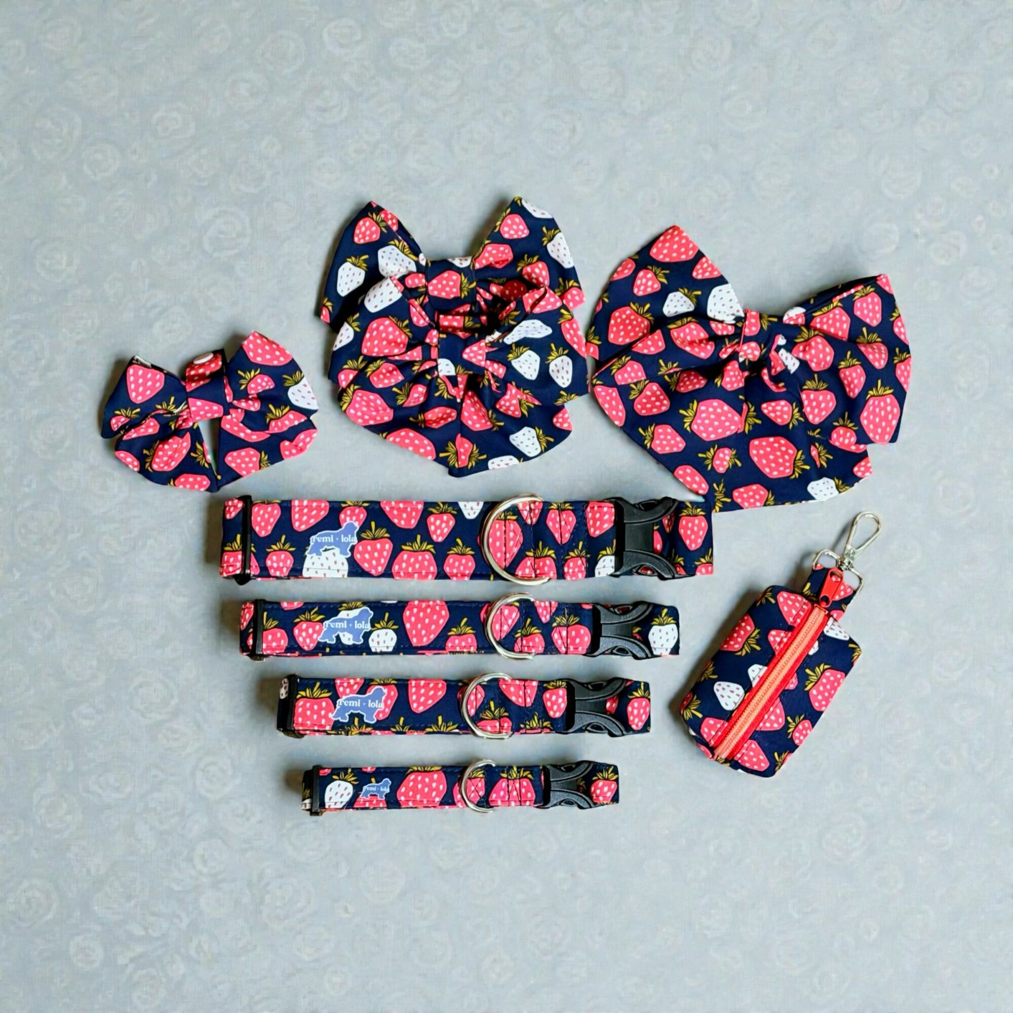 Set of strawberry-patterned pet accessories including bows, collars, a leash, and a small bag, arranged on a light background.