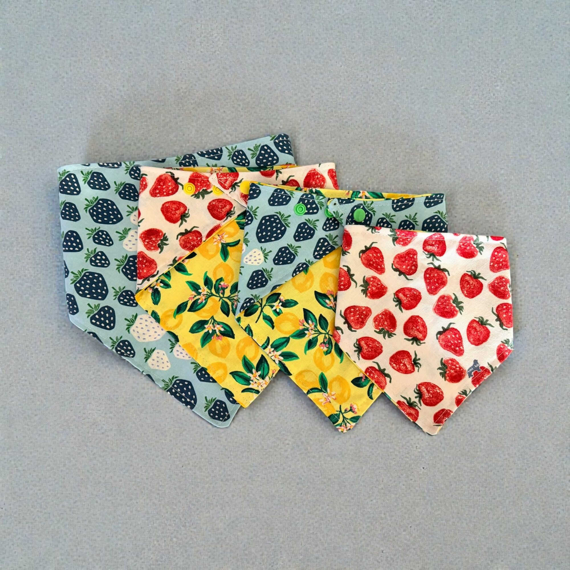 Four fabric face masks with strawberry, blueberry, and lemon patterns, arranged on a gray background.