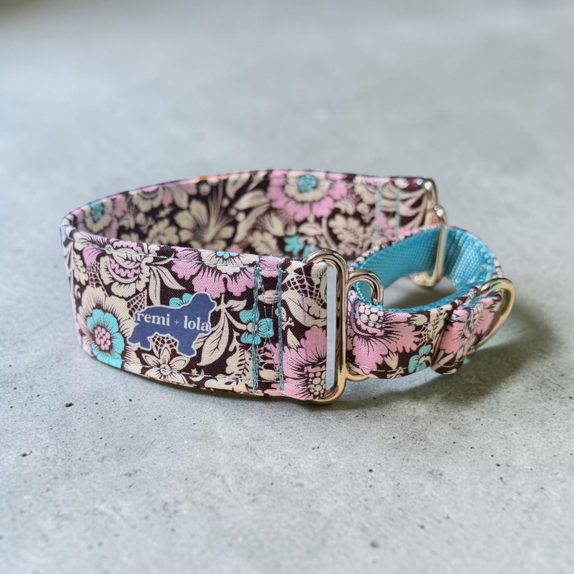 Fabric dog collar with floral pattern, metal buckle, and blue lining, on a gray surface.