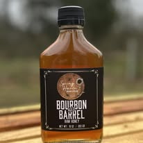 Small bottle of bourbon-flavored syrup with black label and black cap, placed on a wooden surface outdoors.