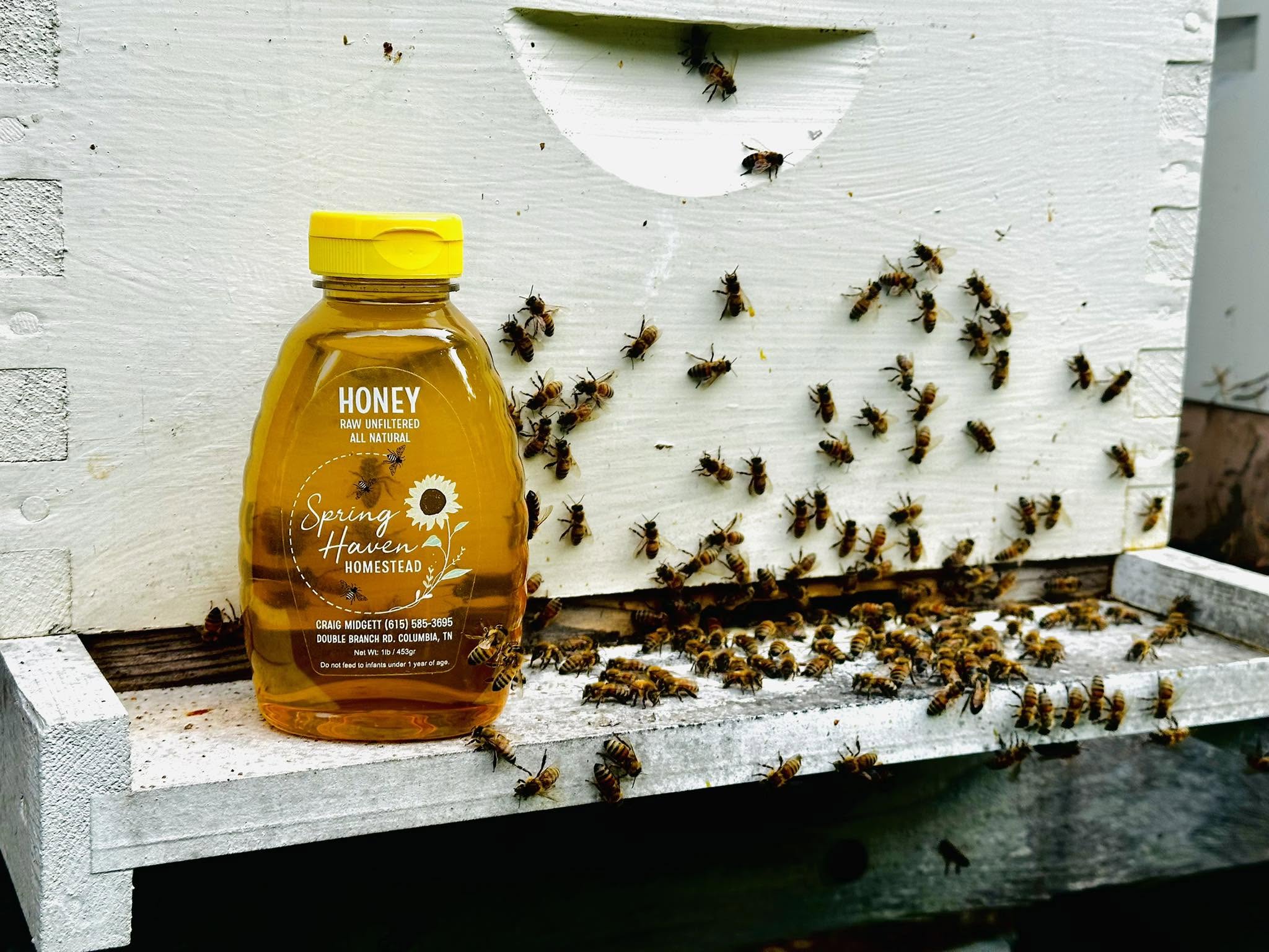 Honey jar on a white hive with bees flying around and entering a small entrance hole, outdoor setting.