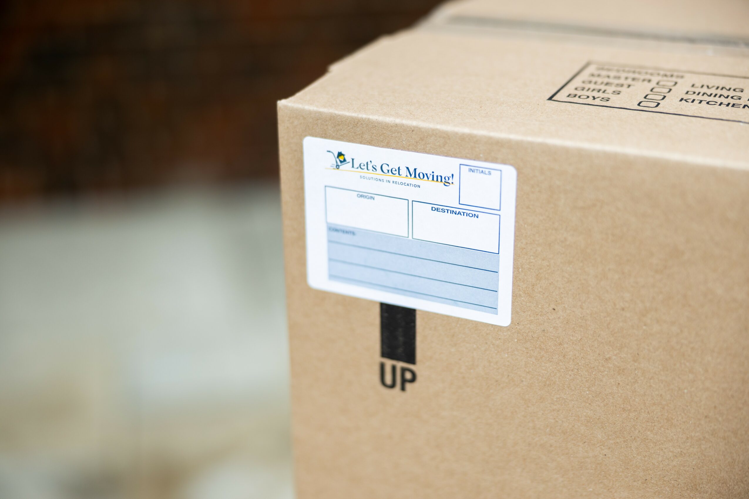 Close-up of a cardboard box with a shipping label and an upward arrow, on a blurred background.