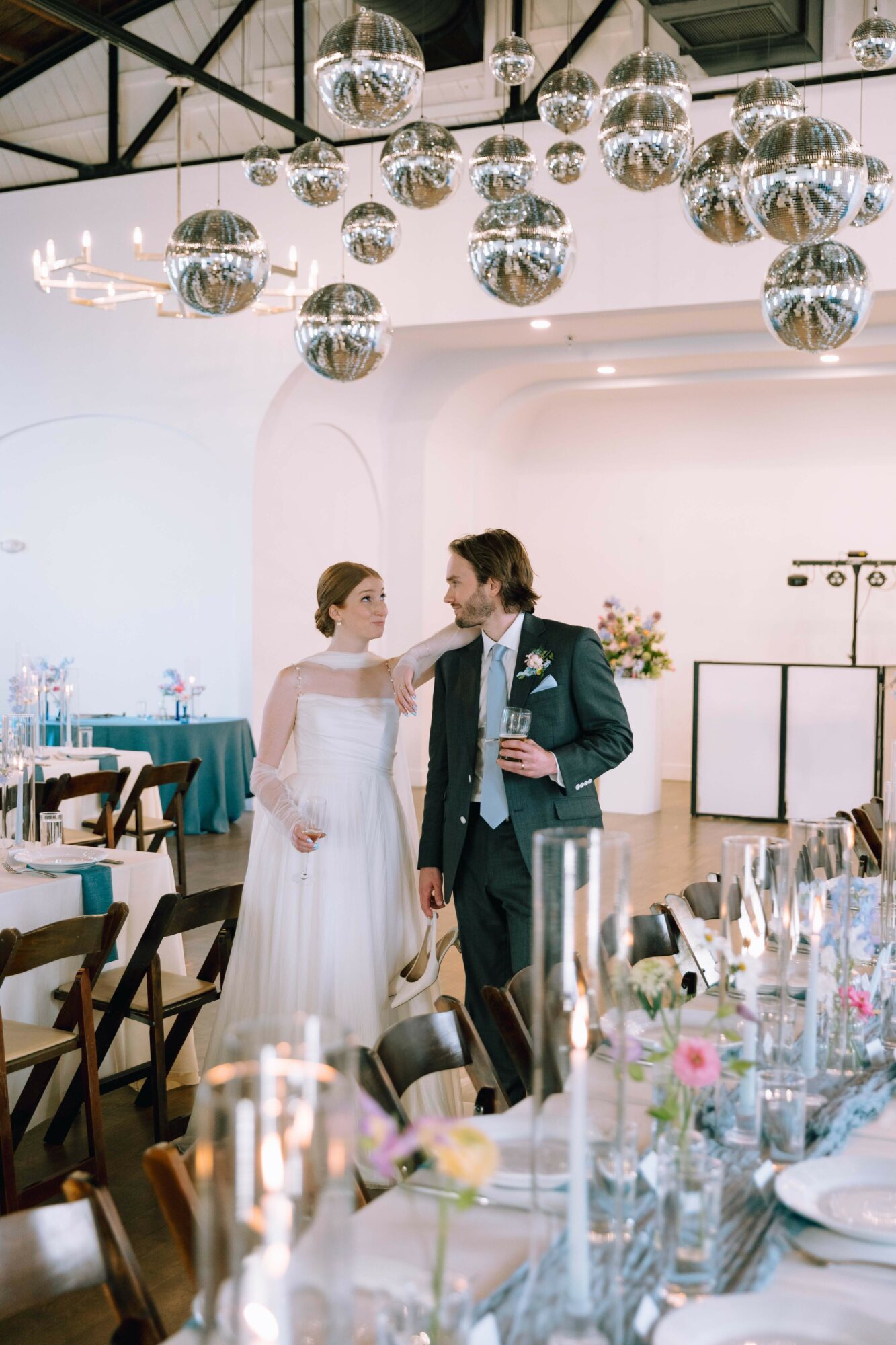 Bride and groom dancing at wedding reception with hanging disco balls and decorated tables.