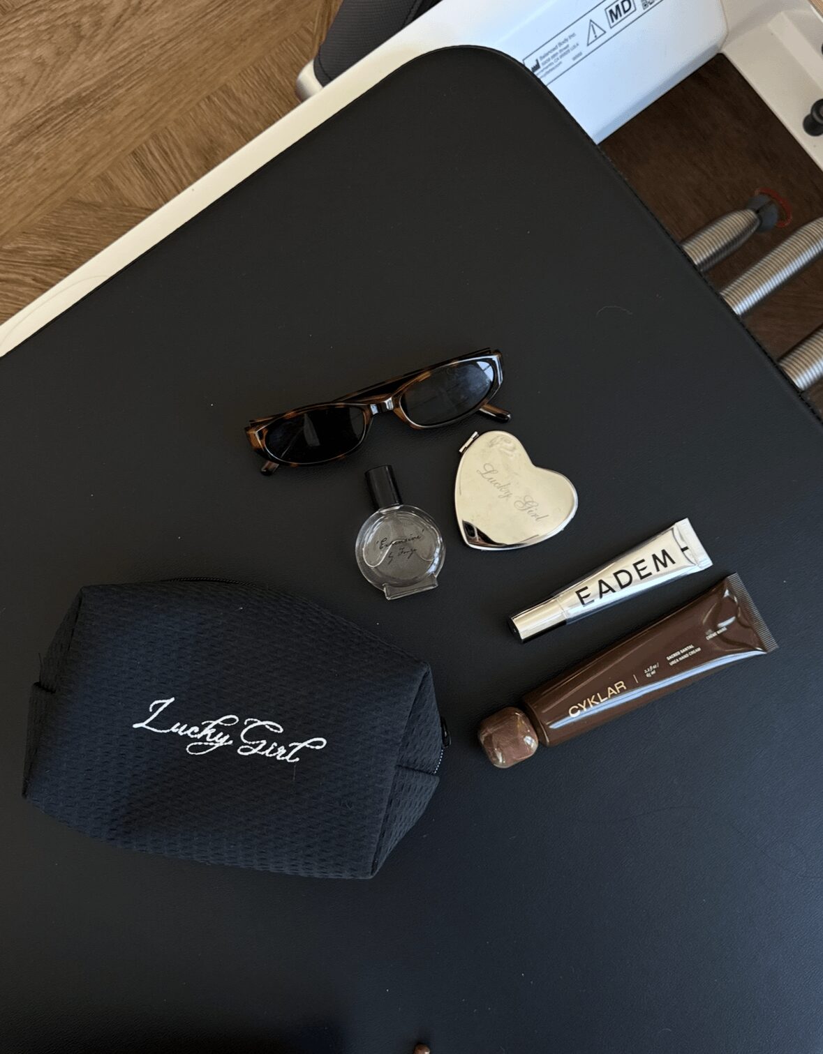 Sunglasses, a watch, a heart-shaped object, a tube of lip balm, and a small black pouch on a black surface.