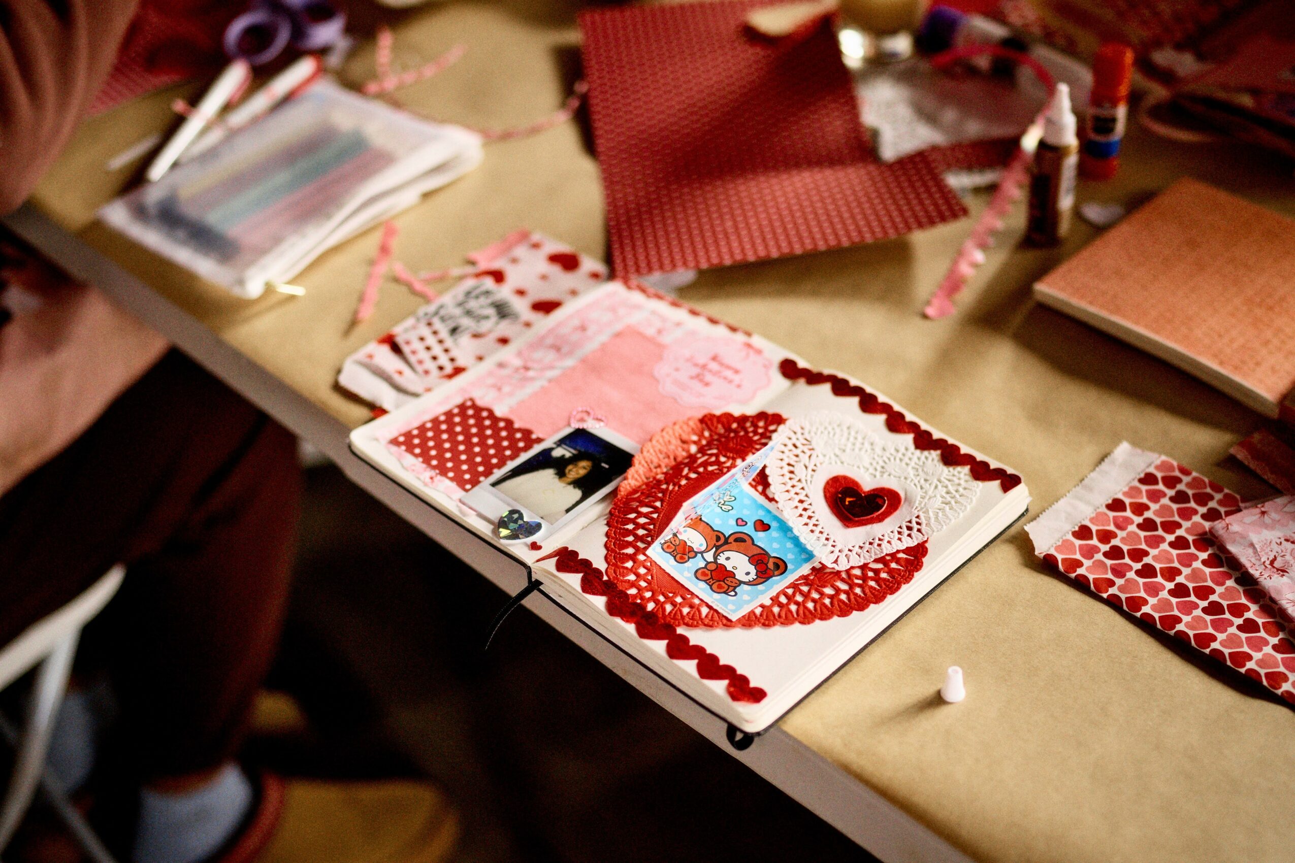 Valentine's Day card with red and white decorations, a heart, and a small photo, on a table with craft supplies.