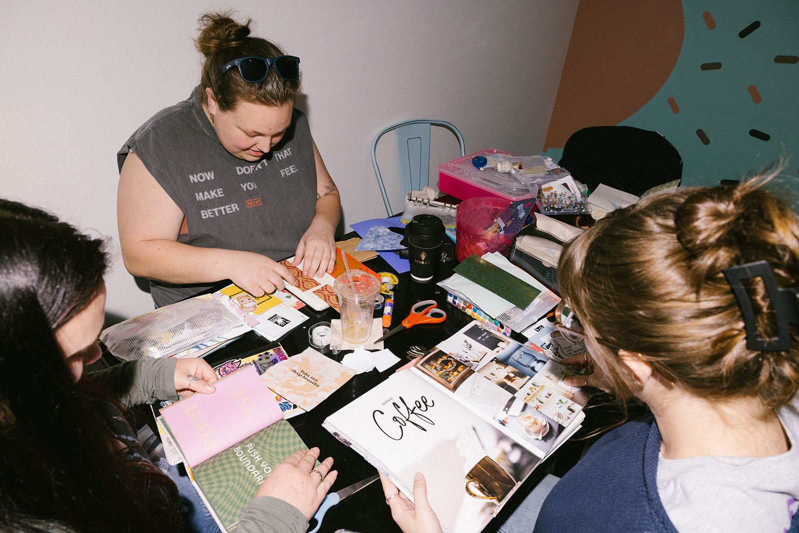 Four people sit around a table with various papers, photos, and supplies, engaged in a creative activity.