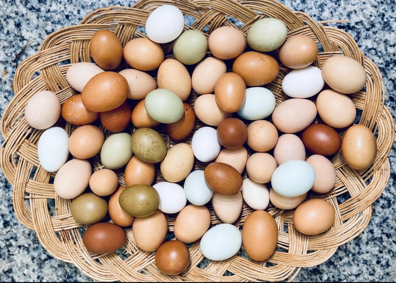 Basket filled with various colored eggs on a textured surface, with a woven pattern. Alt text word count: 20. Confidence: 0.9