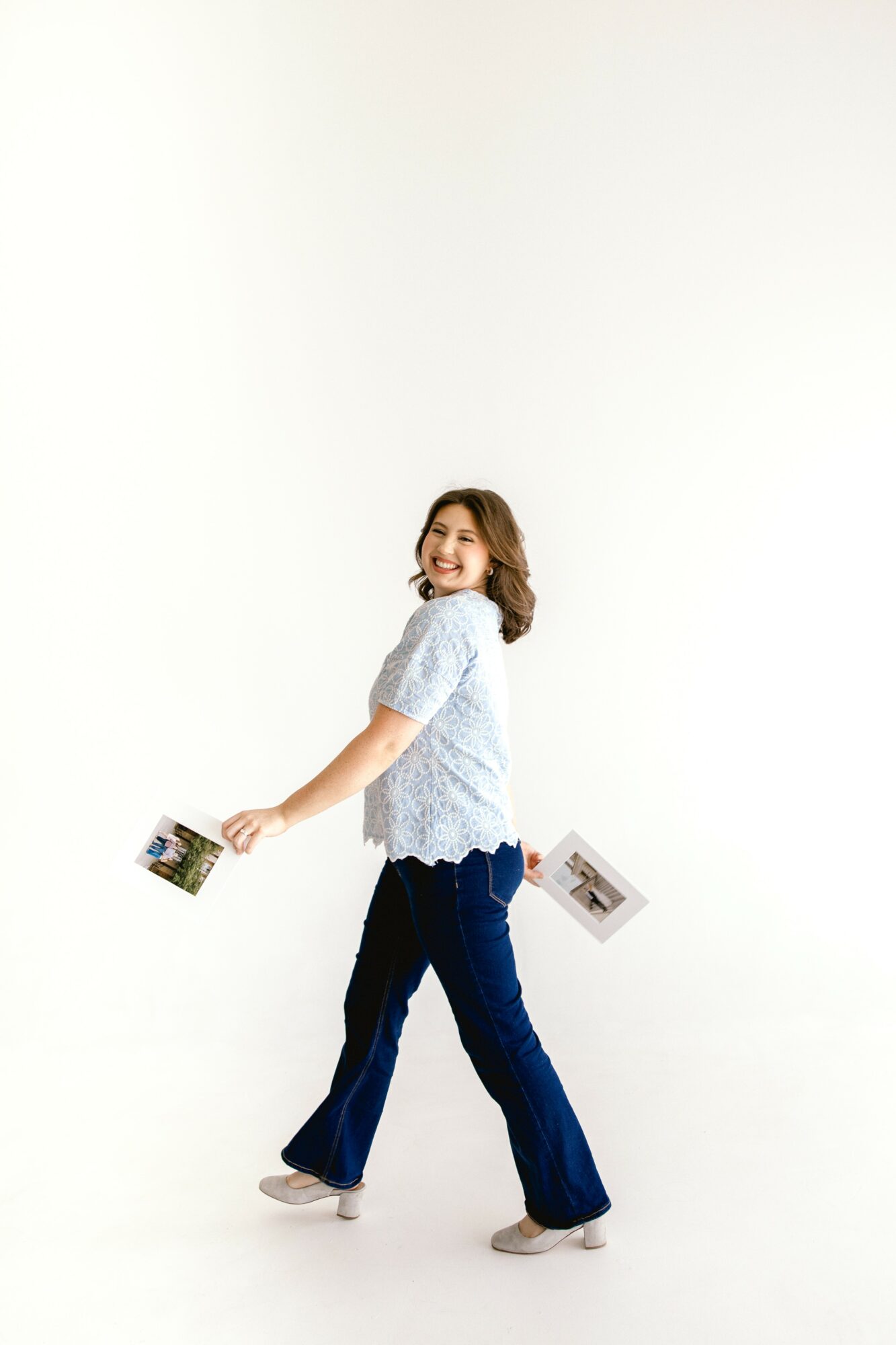 Young woman with short hair smiling, holding a photo in one hand, standing against a plain white background.