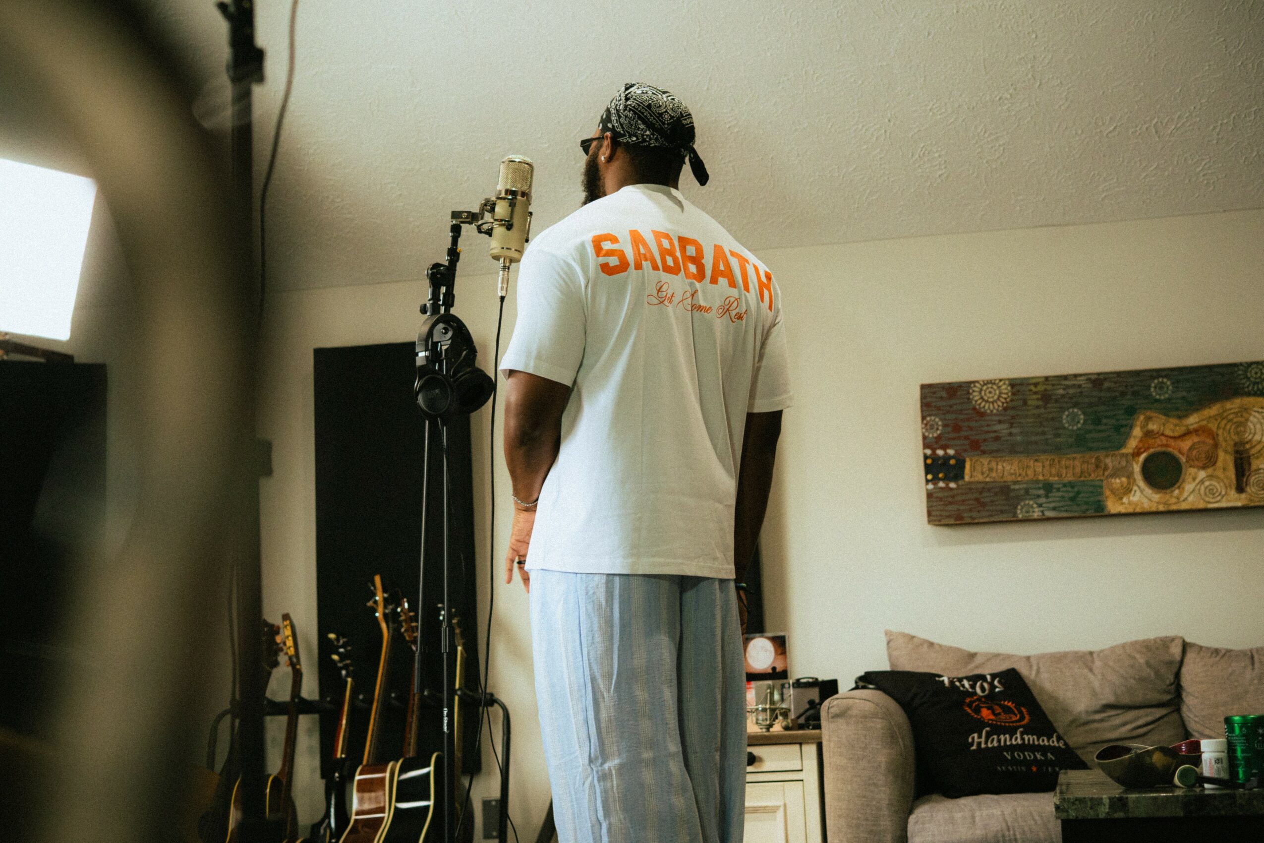 Person with back facing camera, wearing a white T-shirt with orange text, in a room with musical instruments and artwork