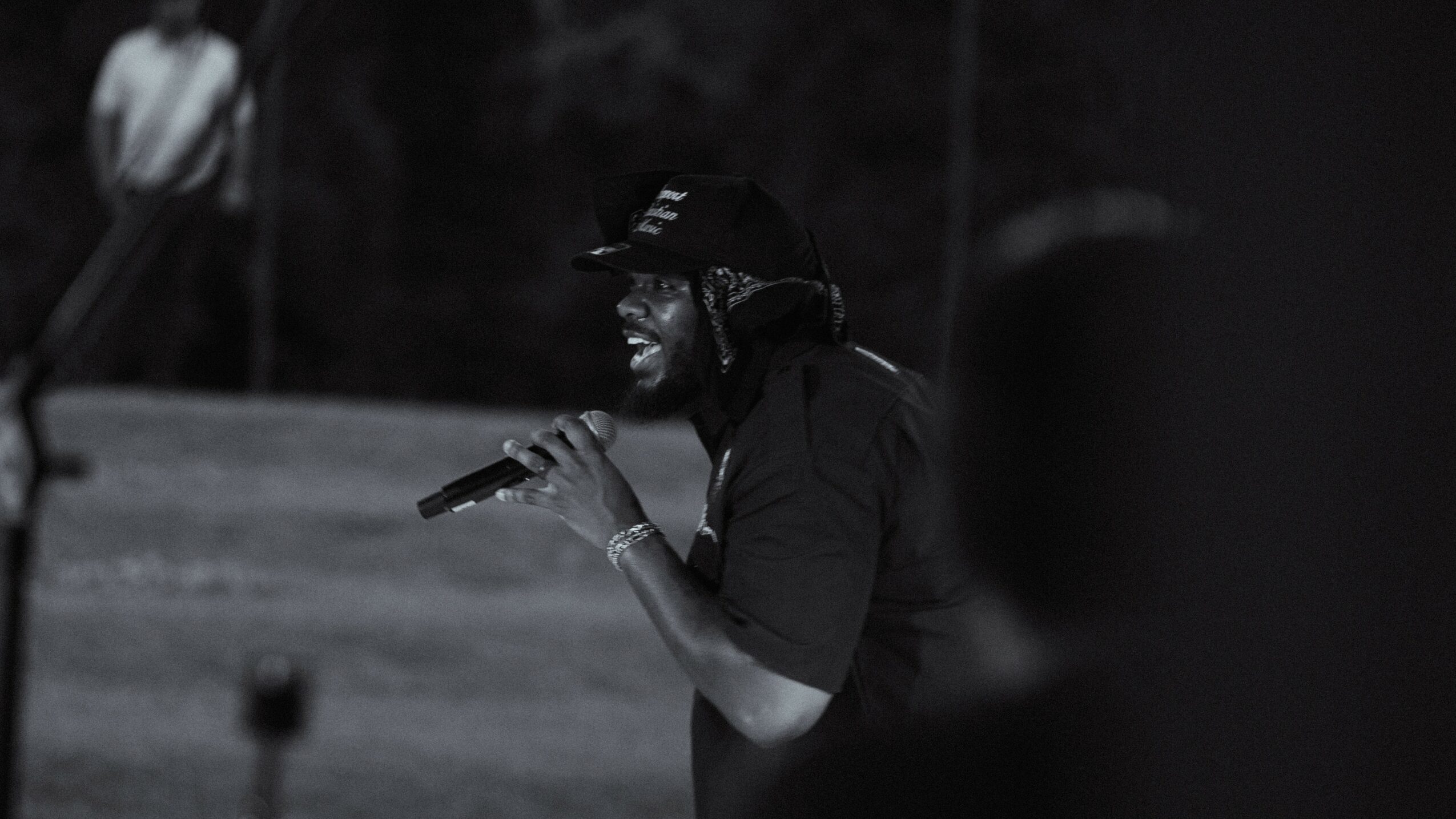 Person singing into a microphone outdoors at night, wearing a cap and dark clothing.