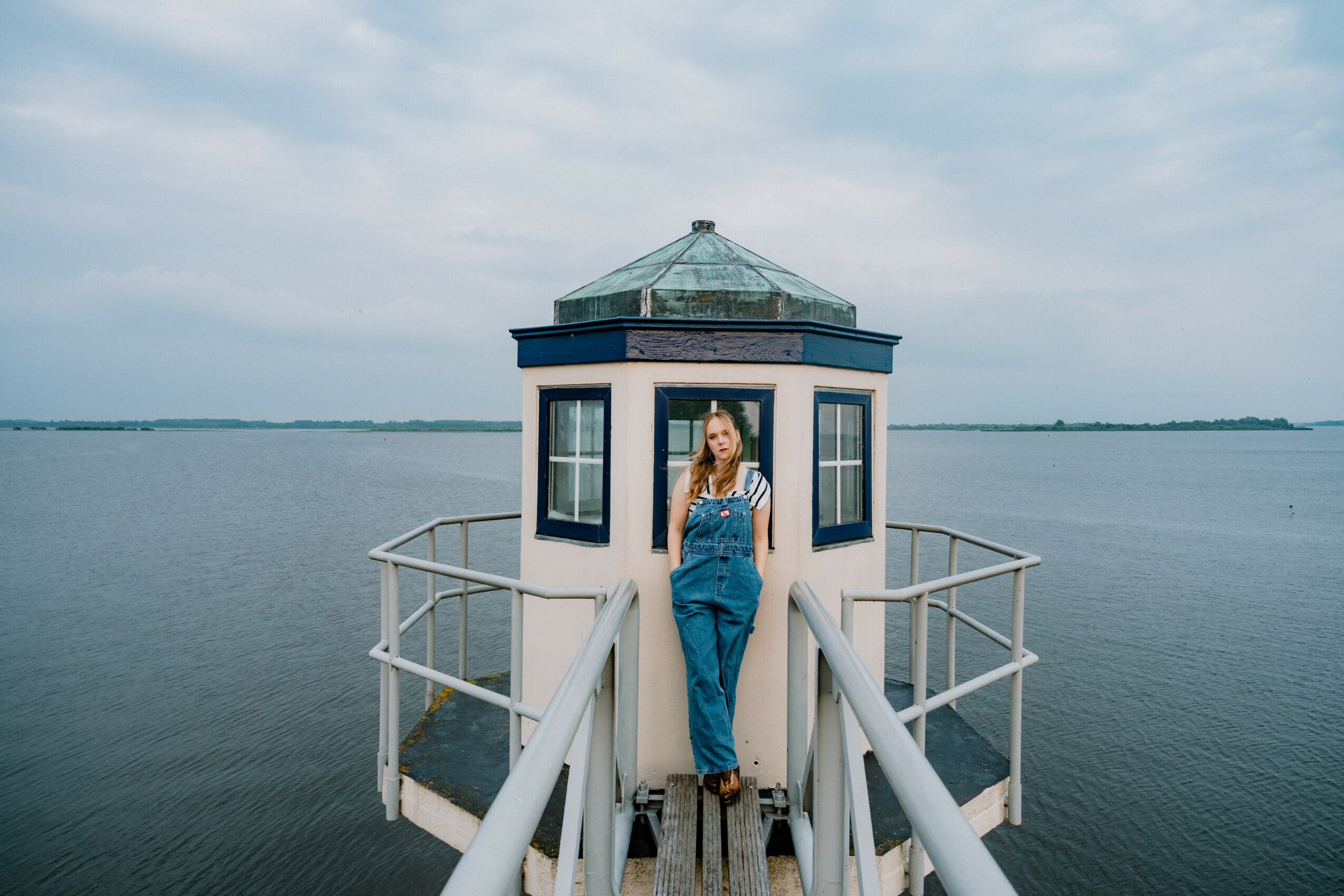 Woman standing on a small lighthouse structure on water, with a cloudy sky background.