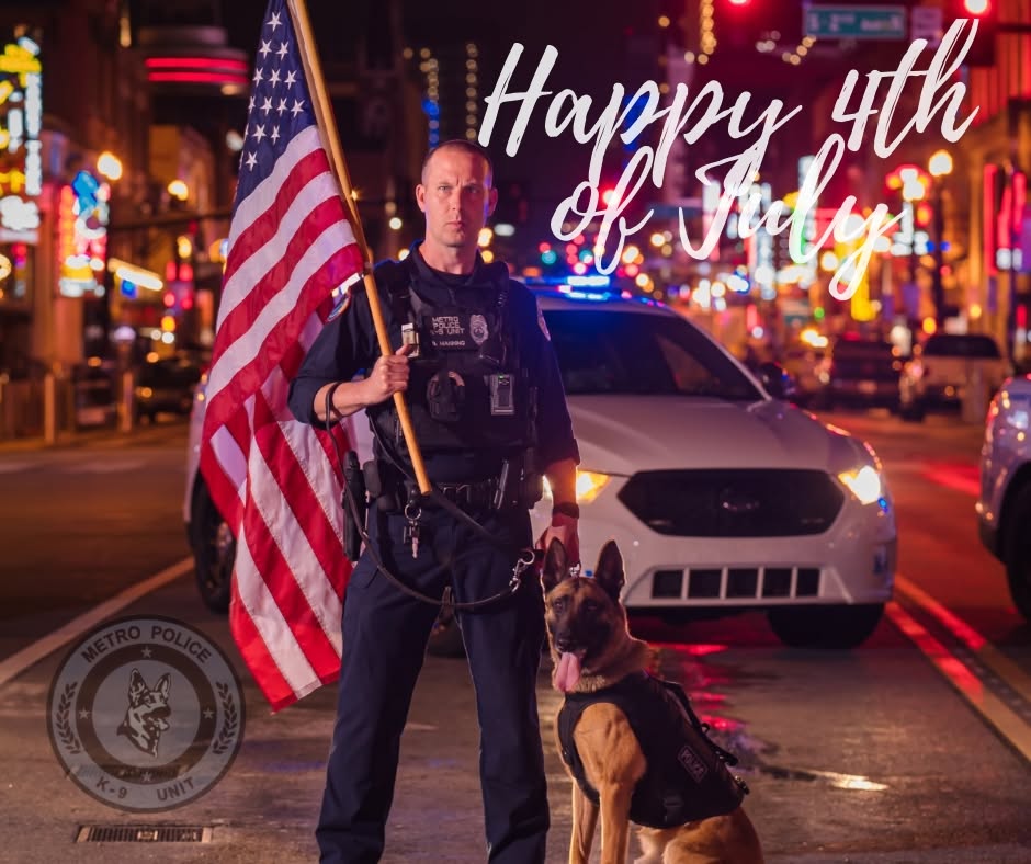 Police officer holding American flag with a police dog in city street at night, with a white car behind, and 'Happy 4th of July' text.