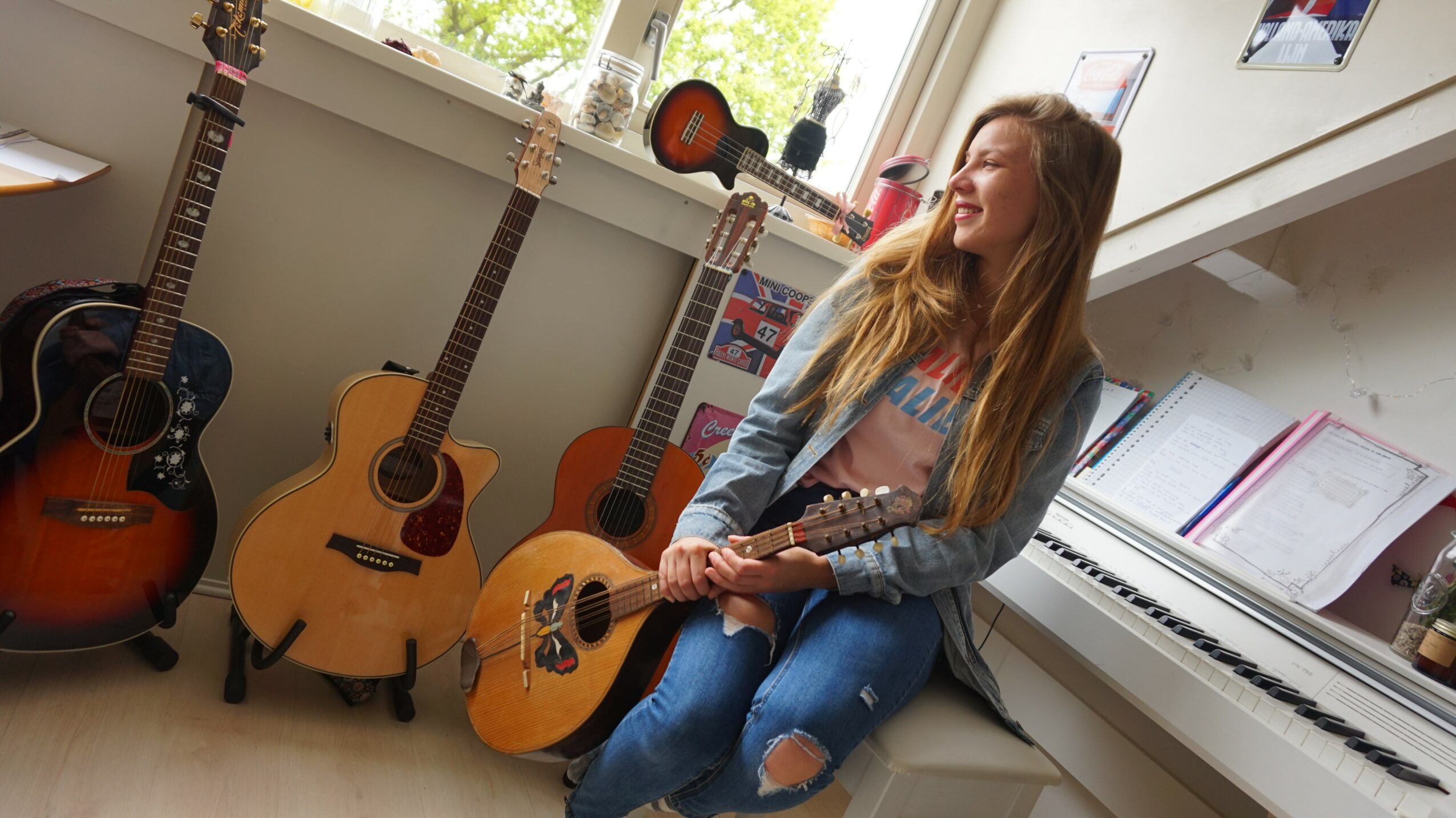 Young woman with long hair sitting on a white bench, holding an acoustic guitar, surrounded by other guitars and a piano.