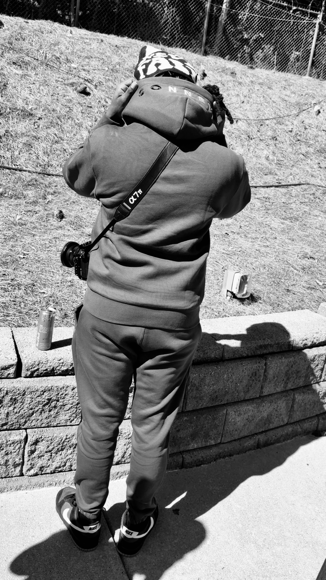 Person carrying a child on shoulders outdoors, standing on a stone ledge, with a grassy hill and fence in background.