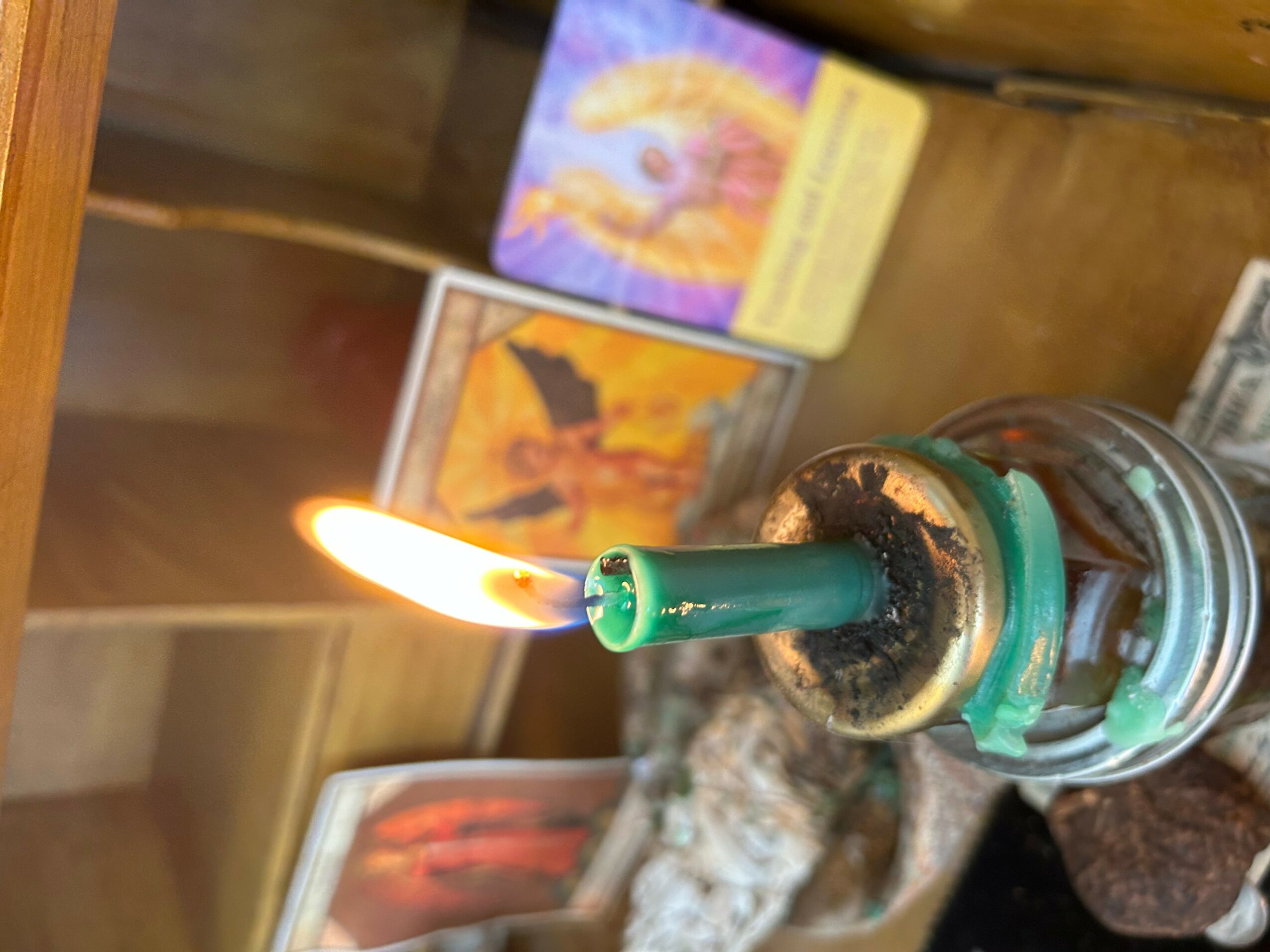 A lit candle with a green wick is burning, with tarot cards and a wooden surface in the background.