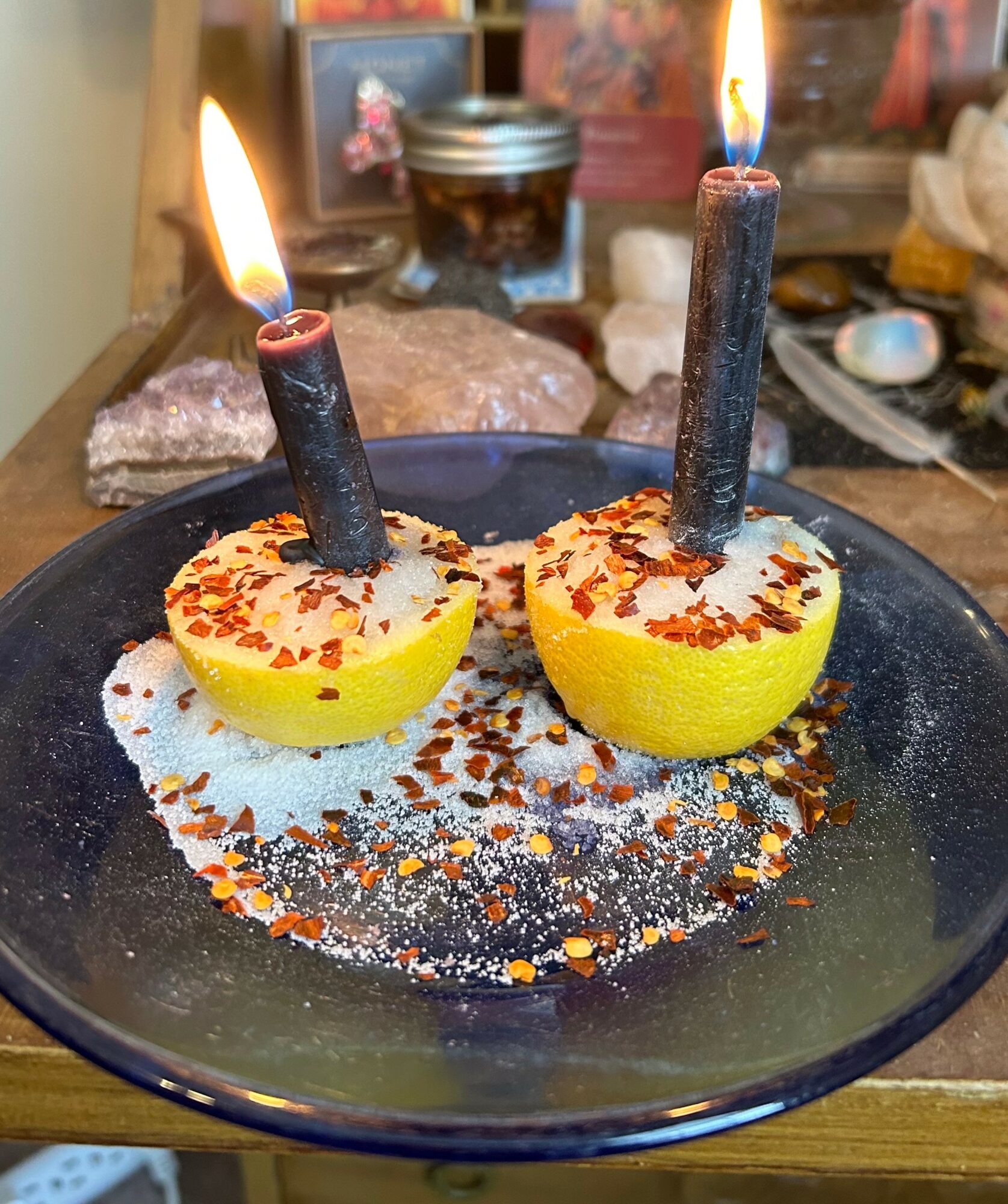 Lemon halves with candles on top, lit and burning, on a black plate with colorful seasoning, in a cluttered background.