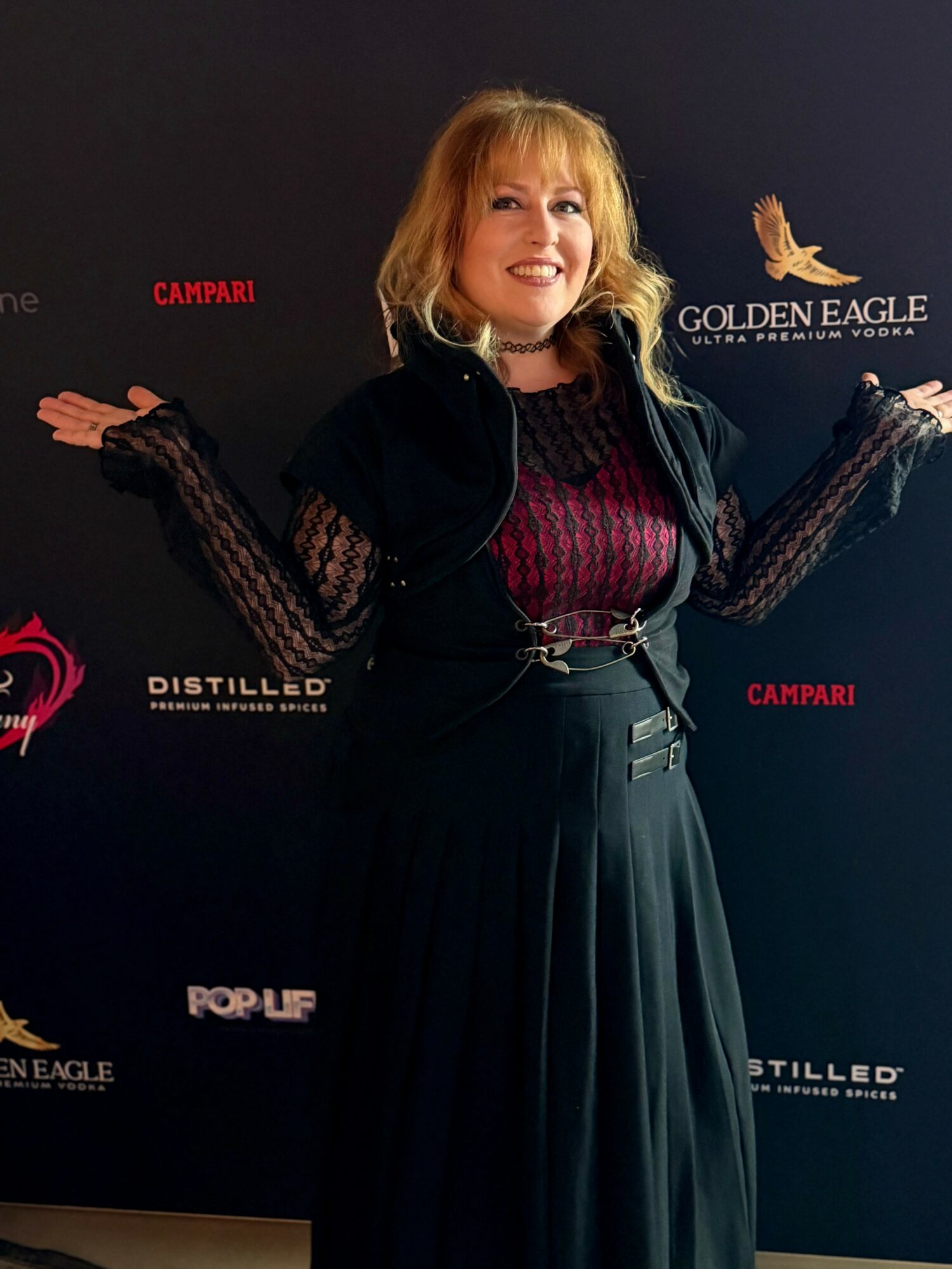 Woman with blonde hair smiling, standing in front of a black backdrop with logos, holding a butterfly in her right hand.