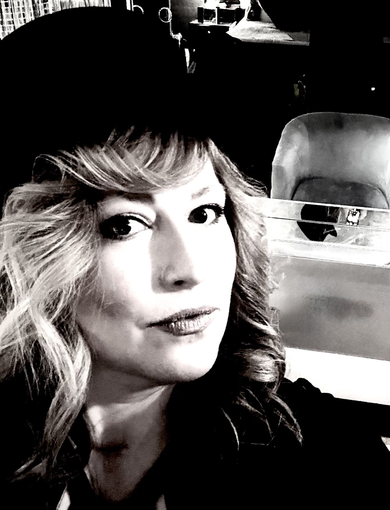 Woman with wavy hair taking a selfie in a car, with a seat and window visible behind her.